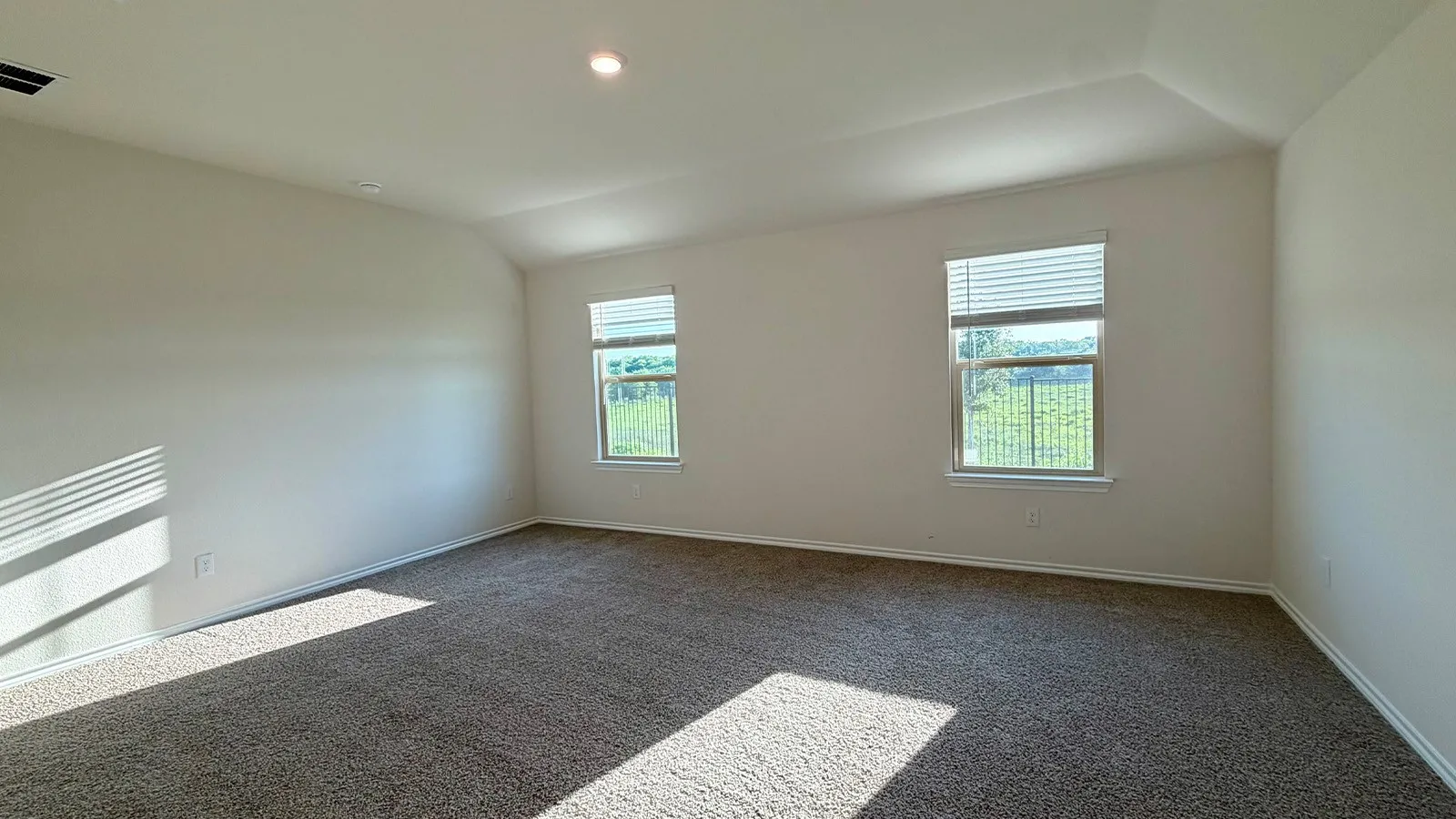 Carpeted room with vaulted ceilings and two windows featuring blinds