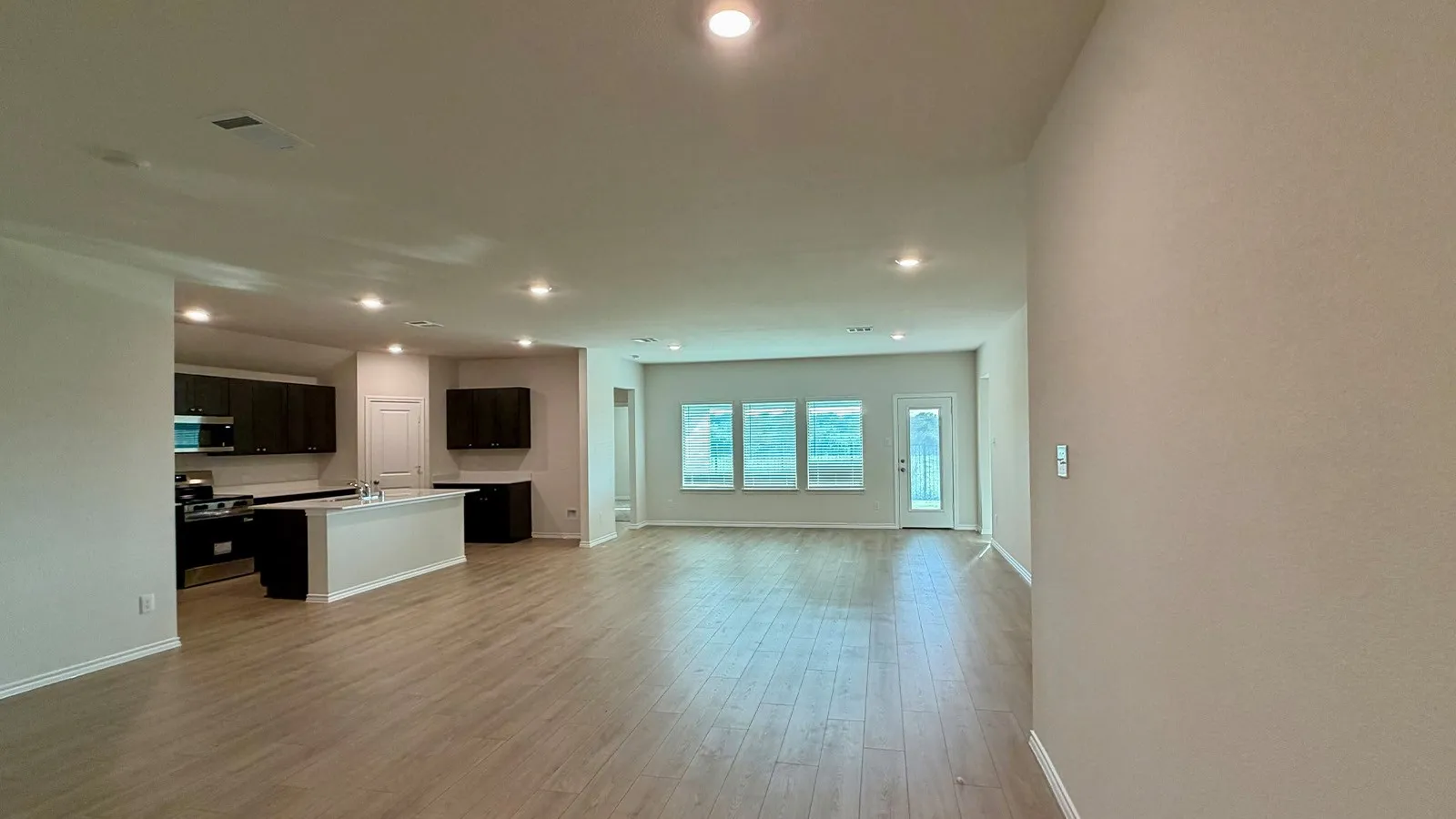 Spacious living area featuring wood-finish flooring, recessed lighting, and a kitchen with dark cabinetry and stainless steel appliances