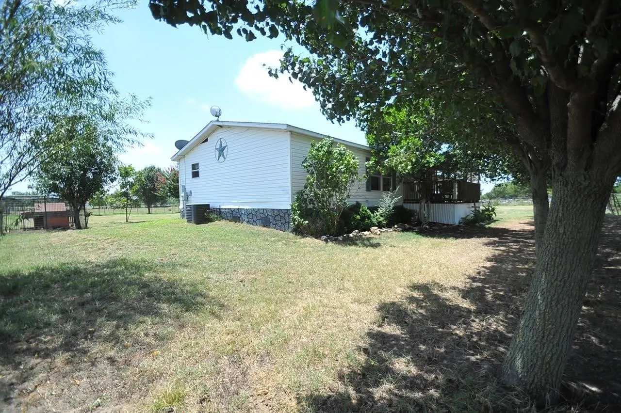 White horizontal siding home with stone foundation accents, a rear deck, and mature trees providing shade