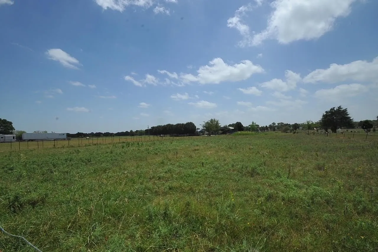 Expansive green pastureland with distant treeline and partial fencing