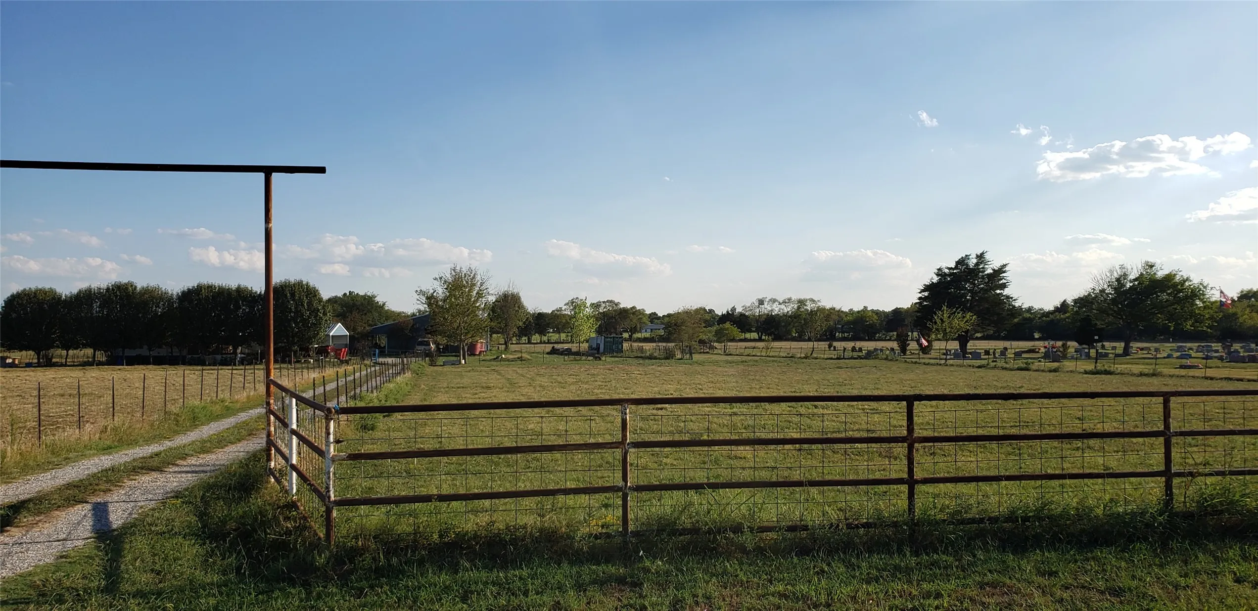 Expansive fenced pastureland featuring a gravel driveway and mature trees