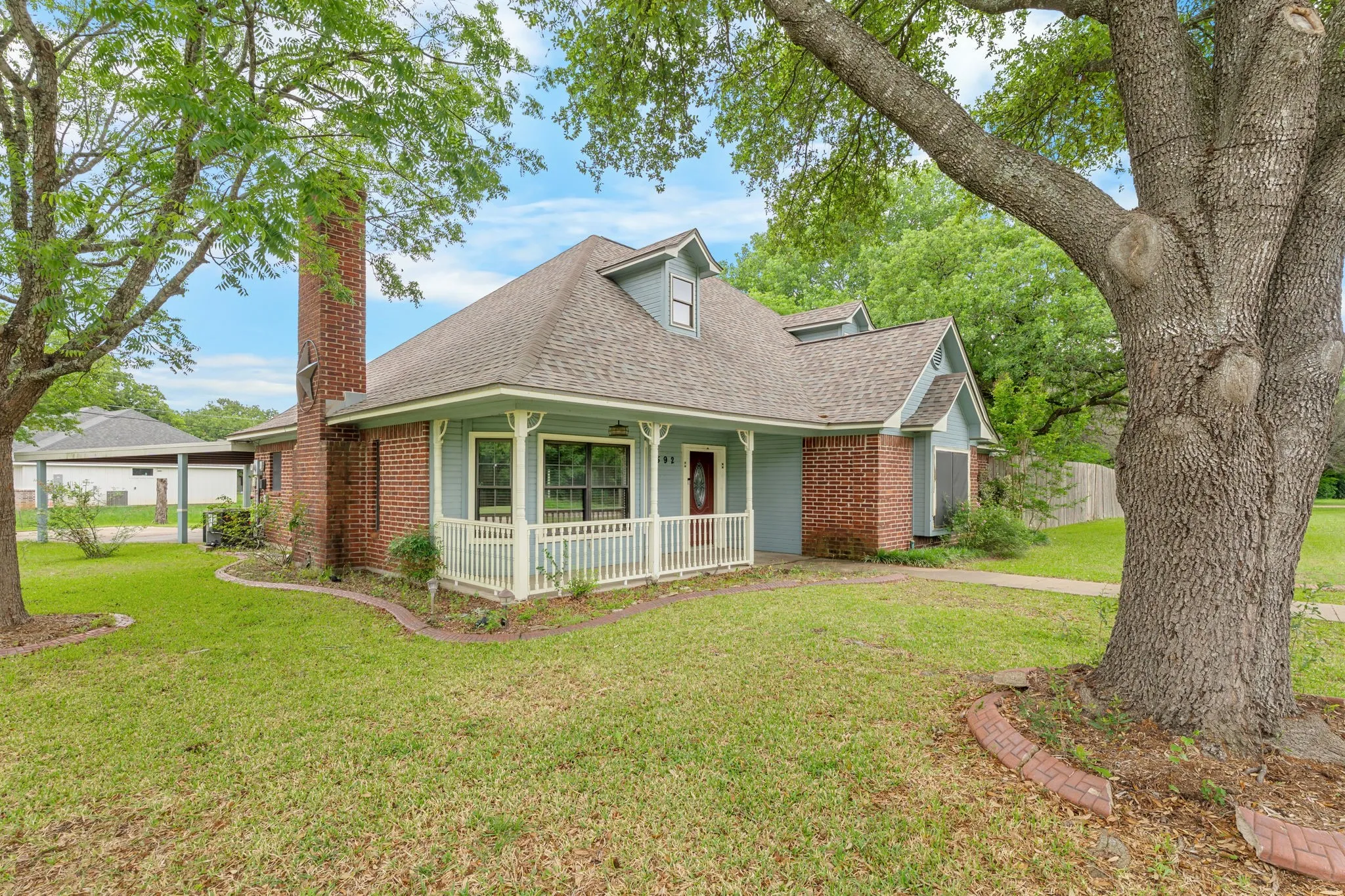 Traditional-style home featuring a red brick facade, light blue siding, a covered porch with white railings, a prominent brick chimney, and a dormer window