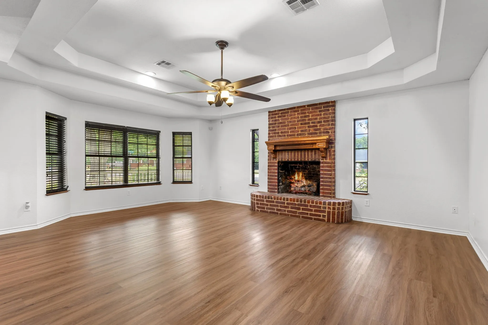 Spacious room featuring wood-finish flooring, a tray ceiling, and a ceiling fan with integrated lighting