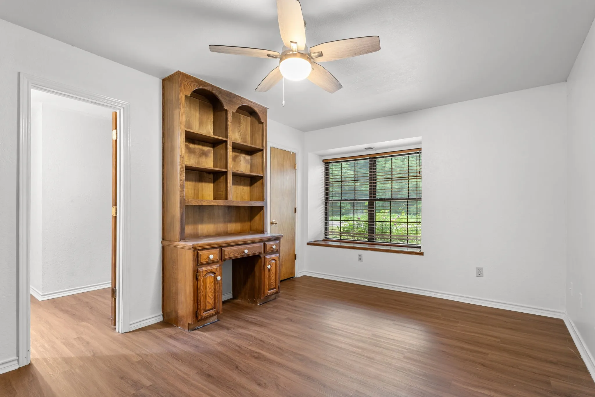 Interior room featuring wood-finish flooring and a built-in wooden desk with shelving