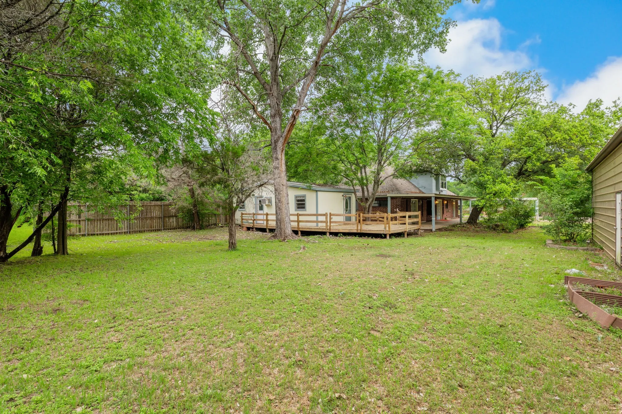 Expansive grassy yard with mature trees, a wooden privacy fence, and a spacious outdoor deck