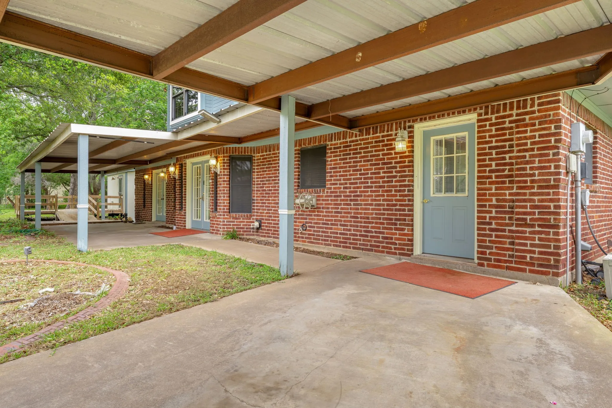 Covered concrete patio extending along the brick exterior, featuring multiple entrances with light blue and off-white doors