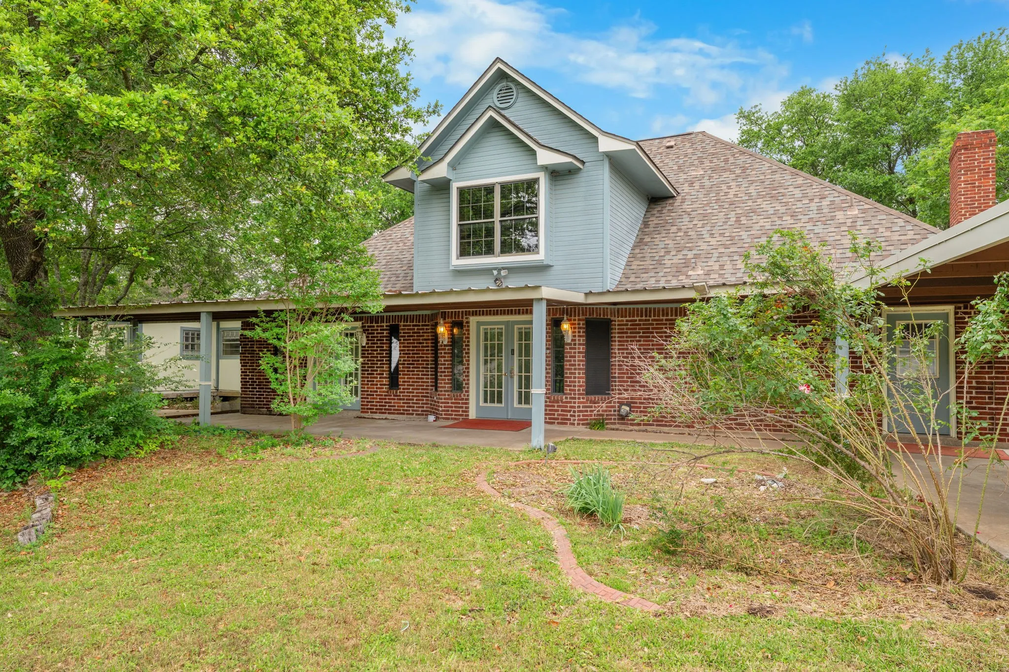 Brick and siding exterior featuring a covered porch, dormer window, and mature trees