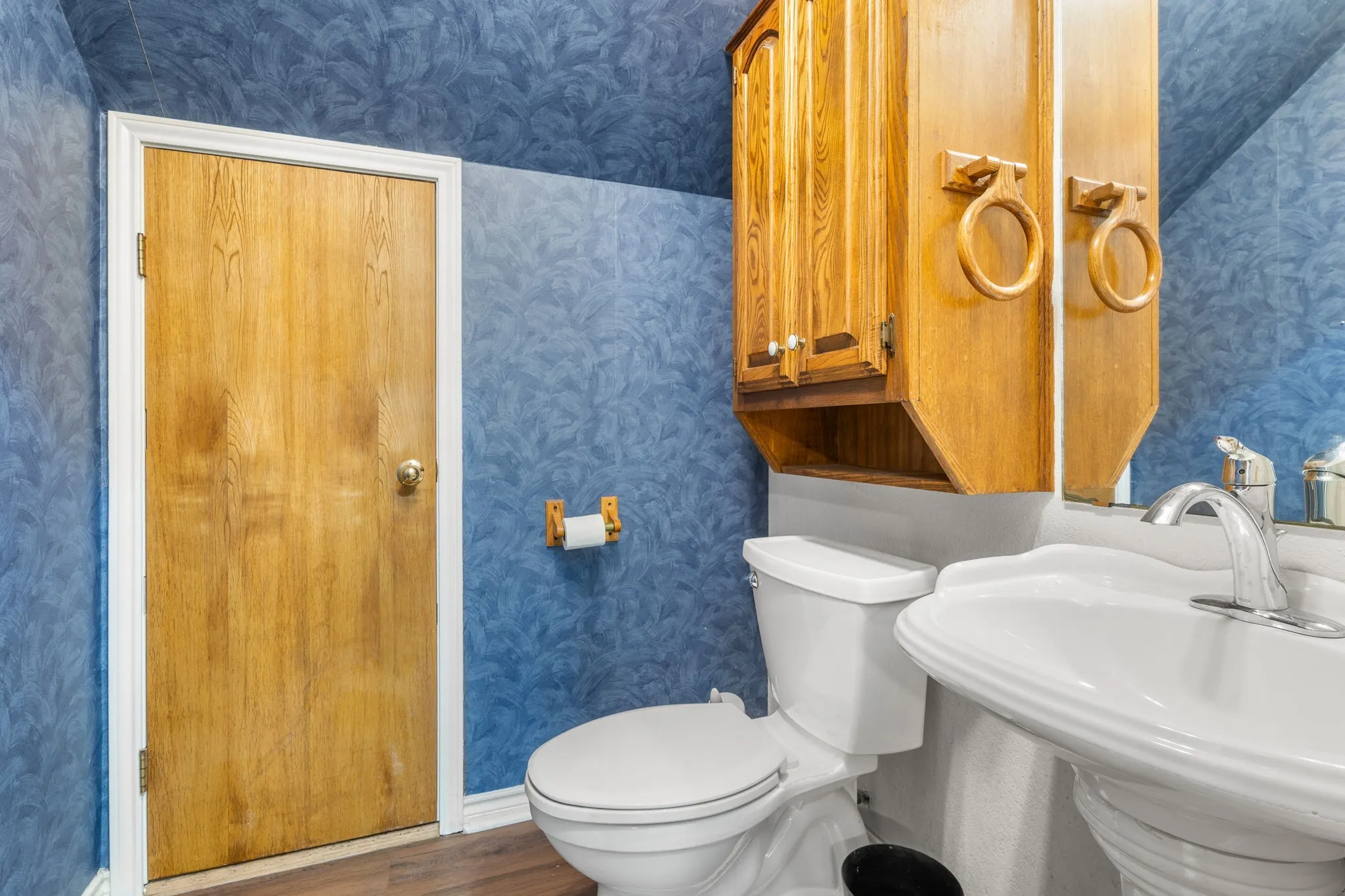 Bathroom featuring a white pedestal sink, built-in wooden cabinetry, and wood-finish flooring