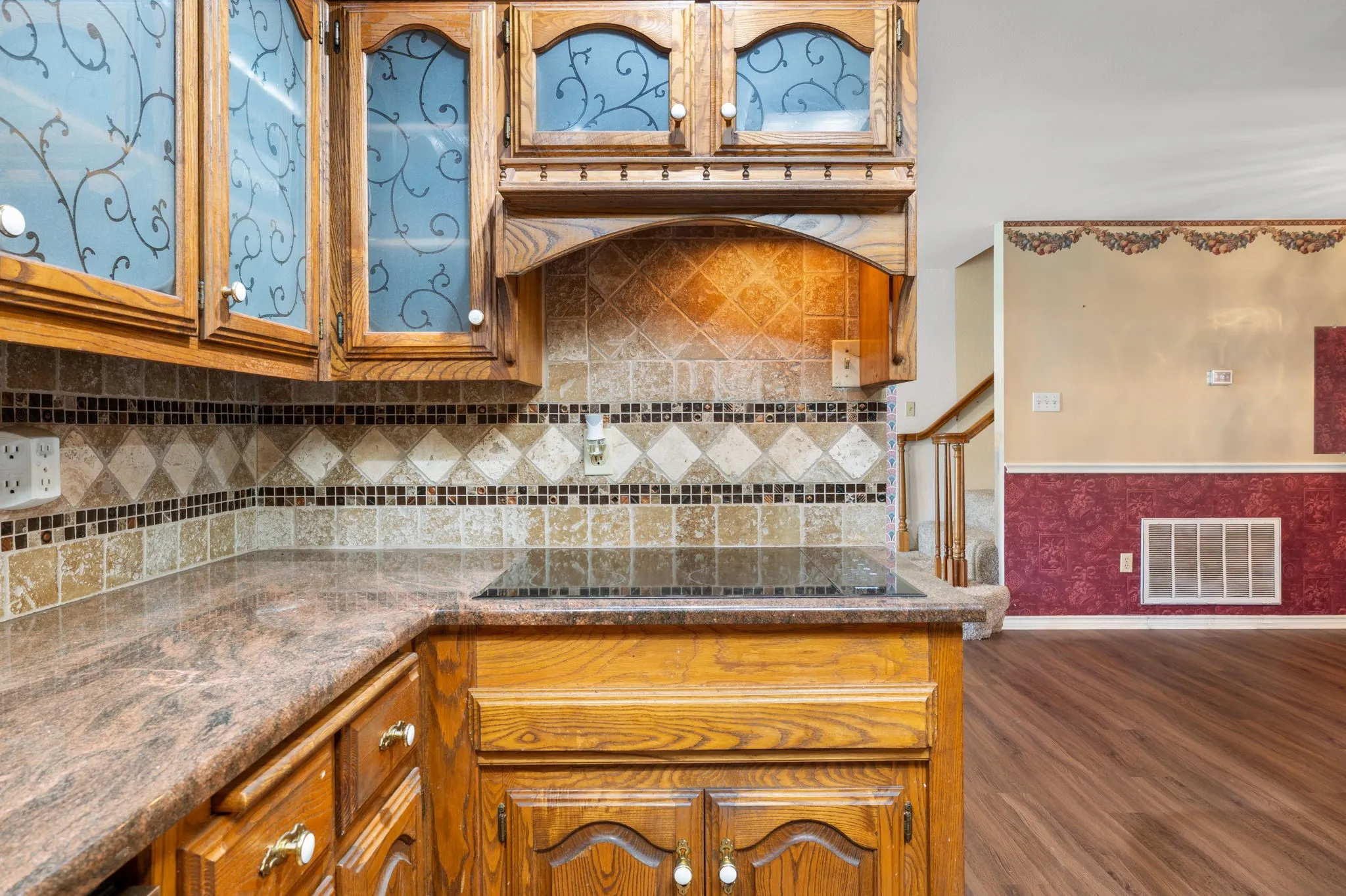 Kitchen featuring wood cabinetry with frosted glass inserts, a built-in cooktop, and a patterned tile backsplash
