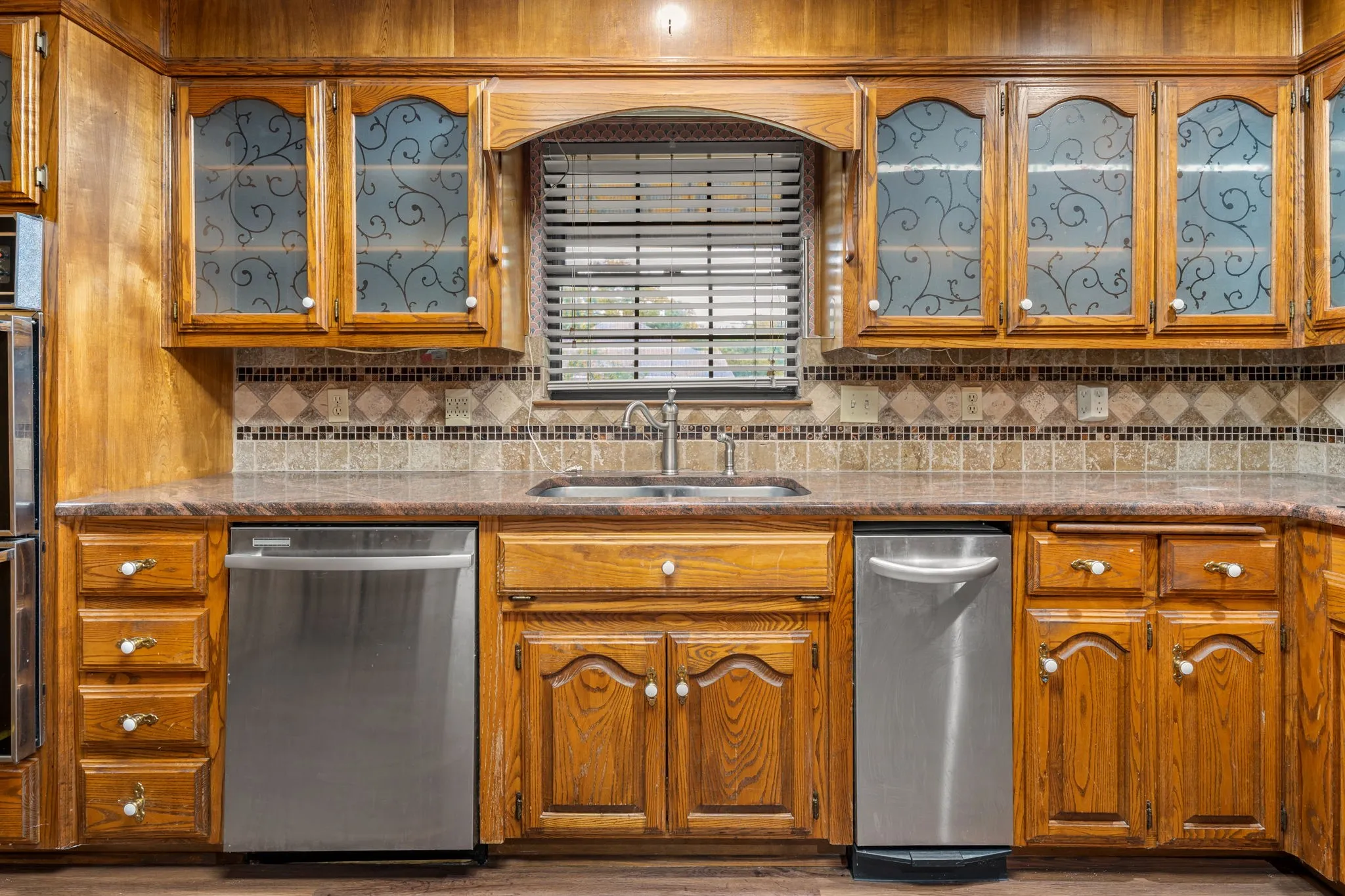 Kitchen featuring wood cabinetry with decorative glass inserts, stainless steel appliances, a mosaic tile backsplash, and composite countertops