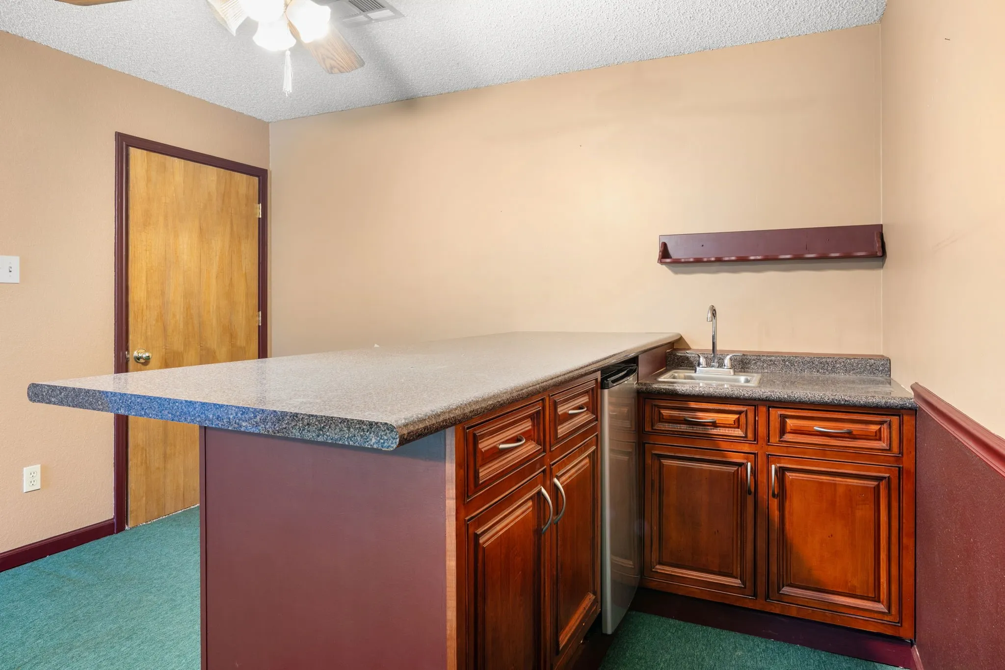 Wet bar area featuring granite-look countertops, rich wood-finish cabinetry, an undermount sink with a chrome faucet, and a built-in beverage refrigerator