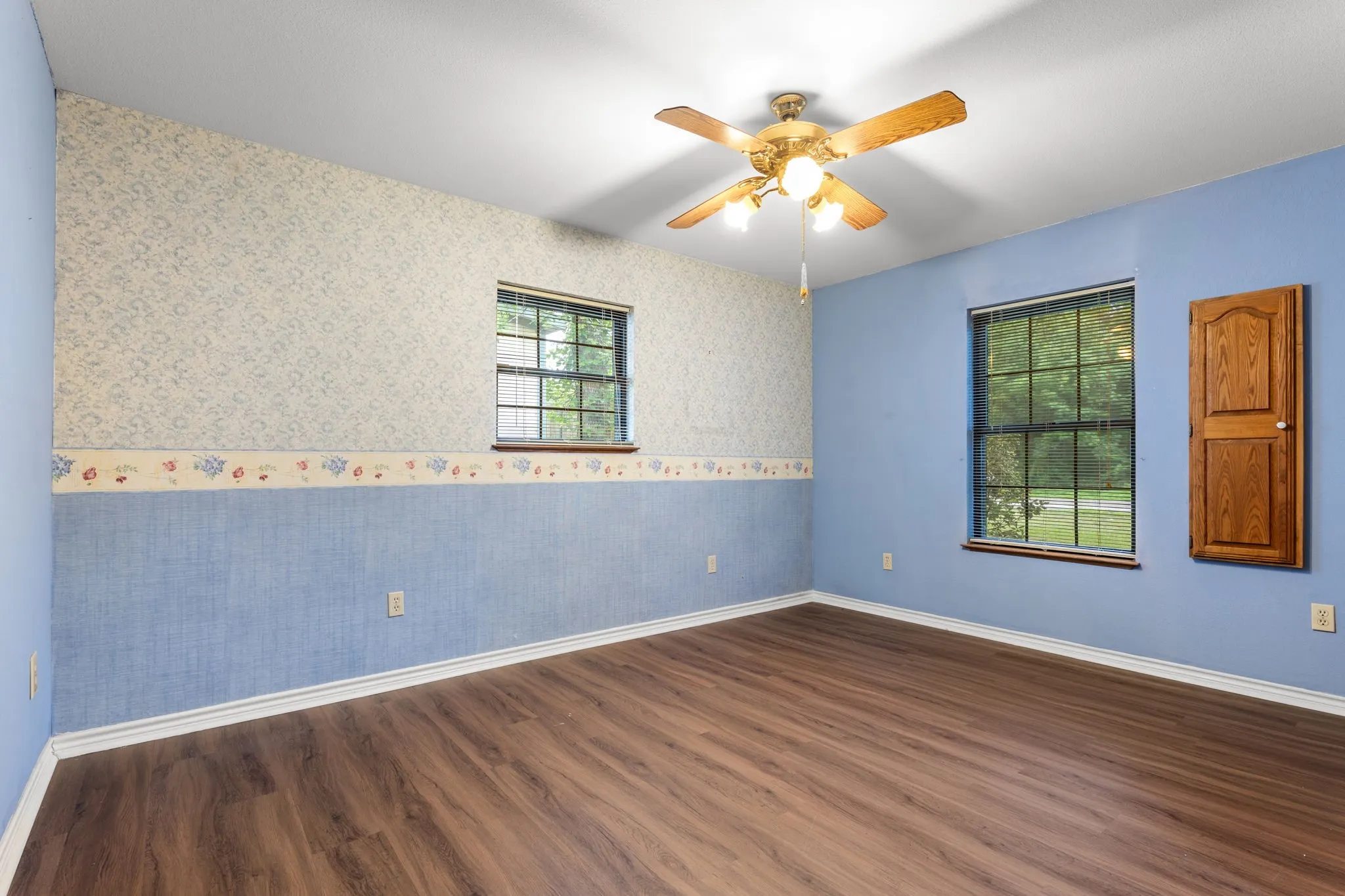 Spacious room featuring wood-finish flooring, two windows, and a ceiling fan with light fixture