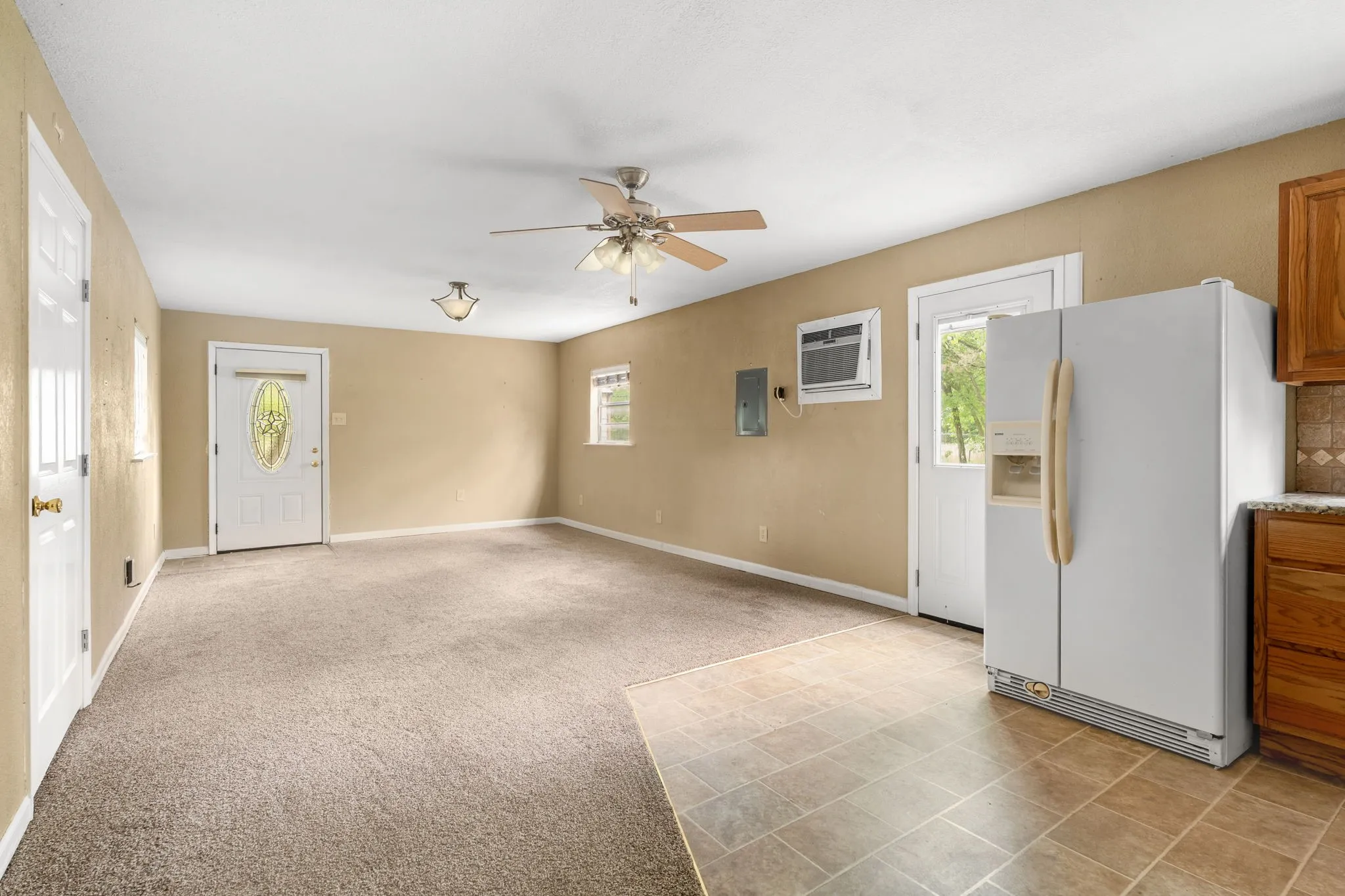 Open-concept interior featuring a ceiling fan with light fixture, neutral carpet, and a white paneled door