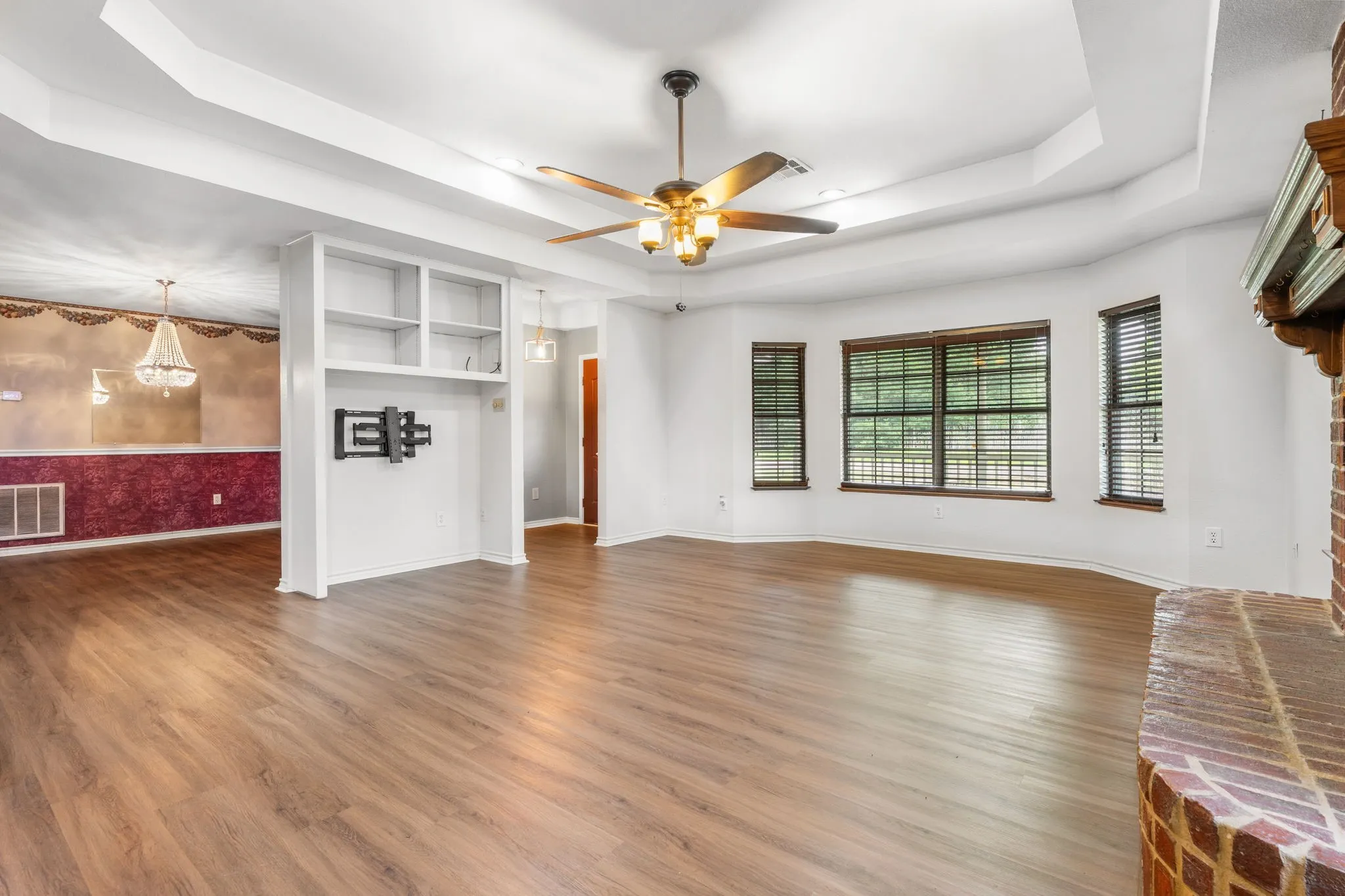 Spacious living area featuring wood-finish flooring, tray ceilings, and a ceiling fan with integrated lighting