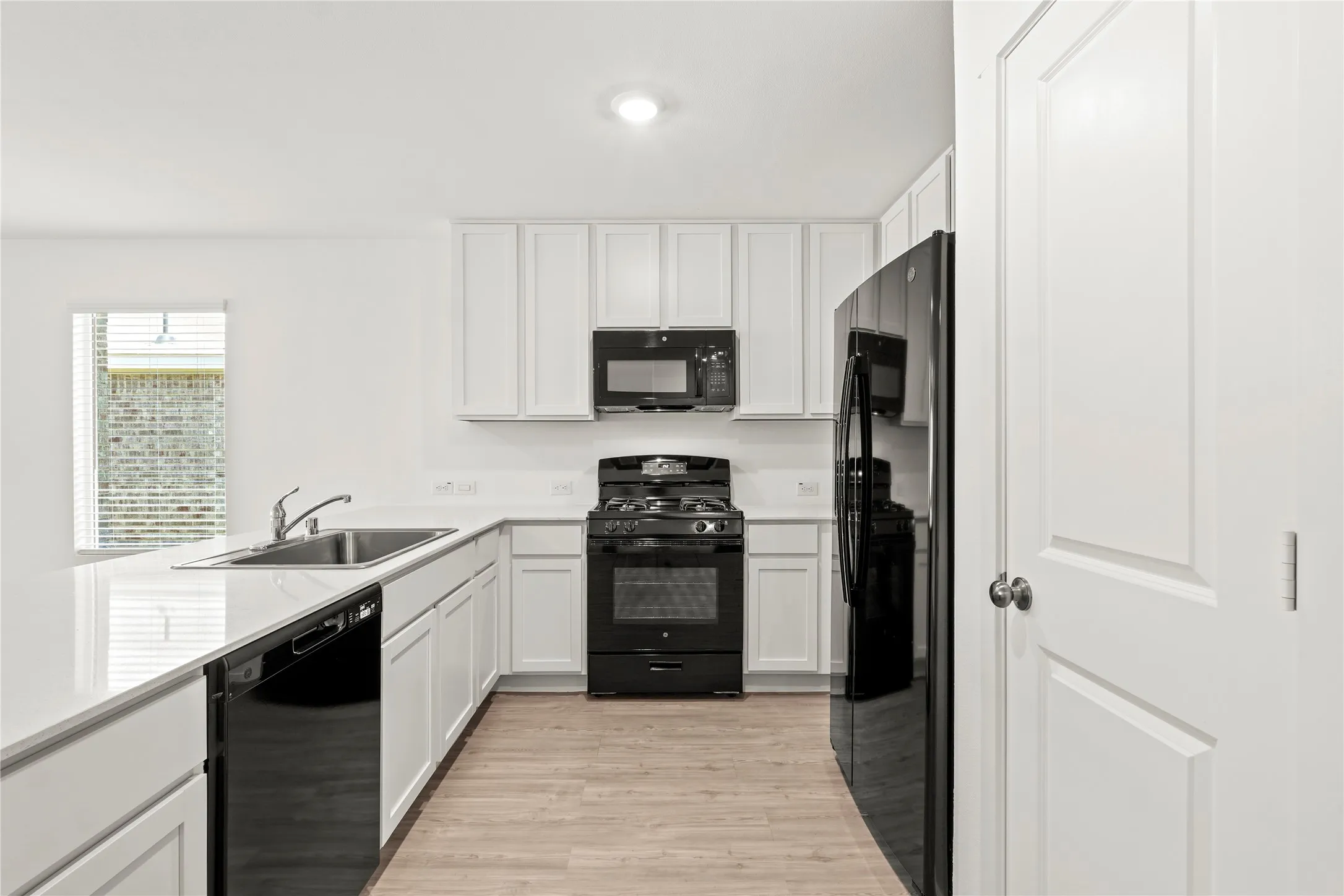 Kitchen featuring white cabinetry, black appliances, a double basin sink, light-toned wood-finish flooring, and white countertops