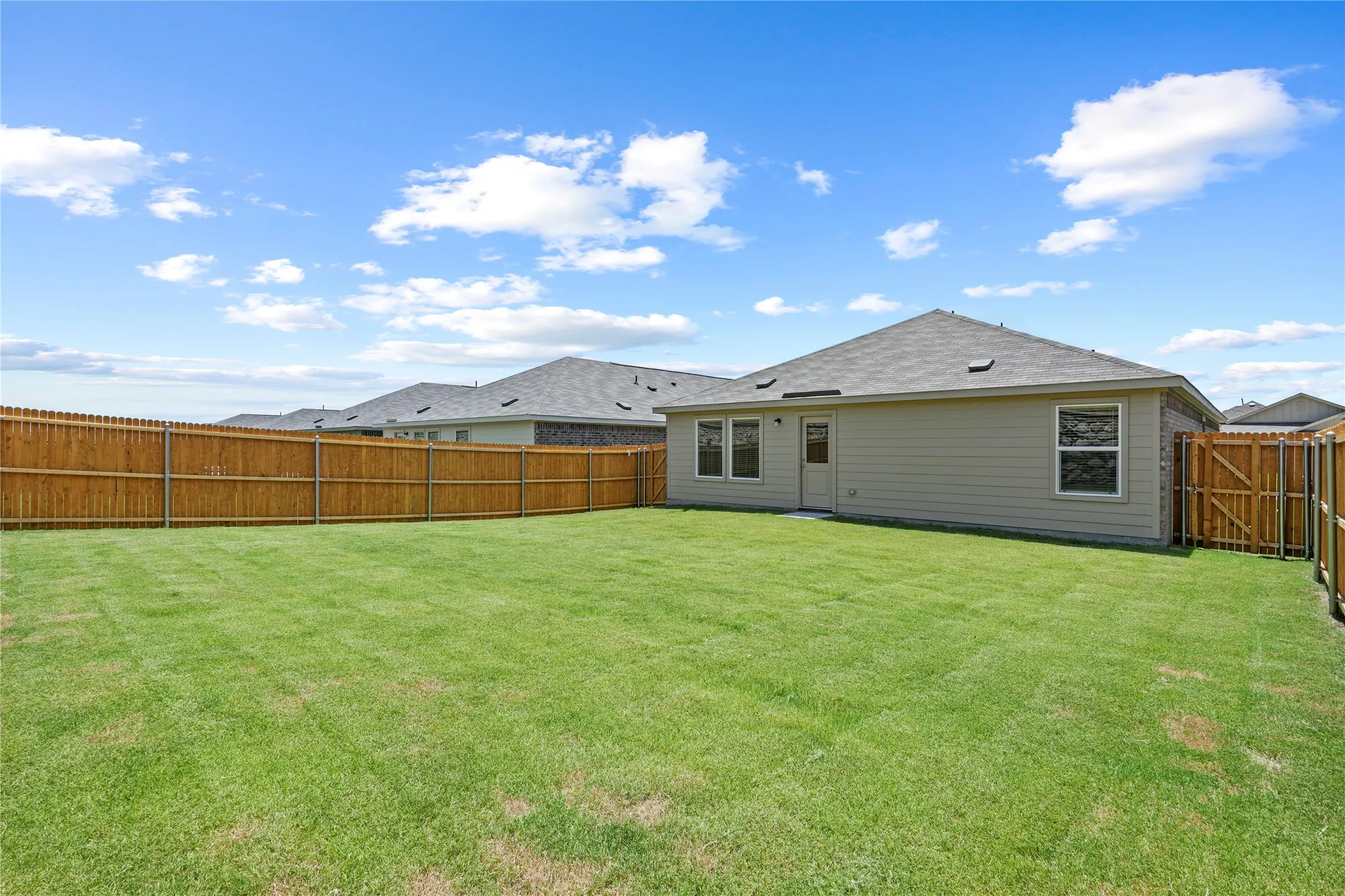 Expansive backyard featuring a lush lawn, complete privacy fencing, and a rear exterior with multiple windows