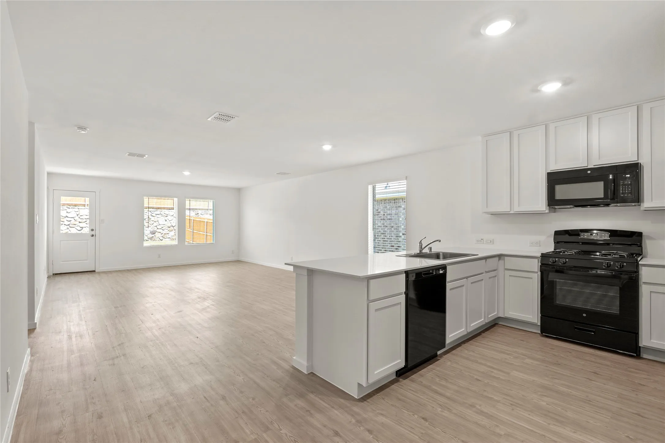 Open-concept kitchen and living area featuring wood-finish flooring, white cabinetry, a kitchen island with sink, and black appliances