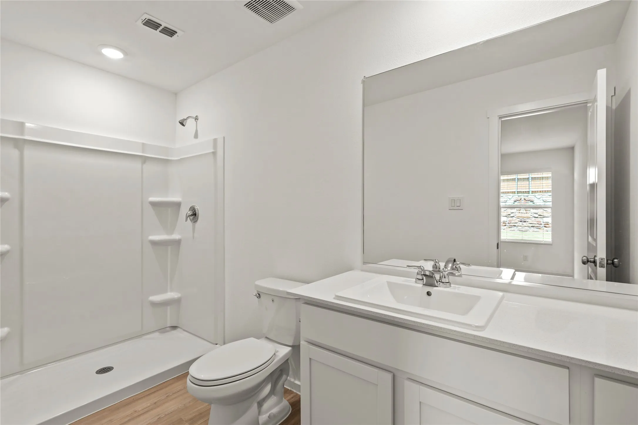 Full bathroom featuring a single-basin vanity with a white countertop, a large wall-mounted mirror, a commode, a shower enclosure, and wood-finish flooring