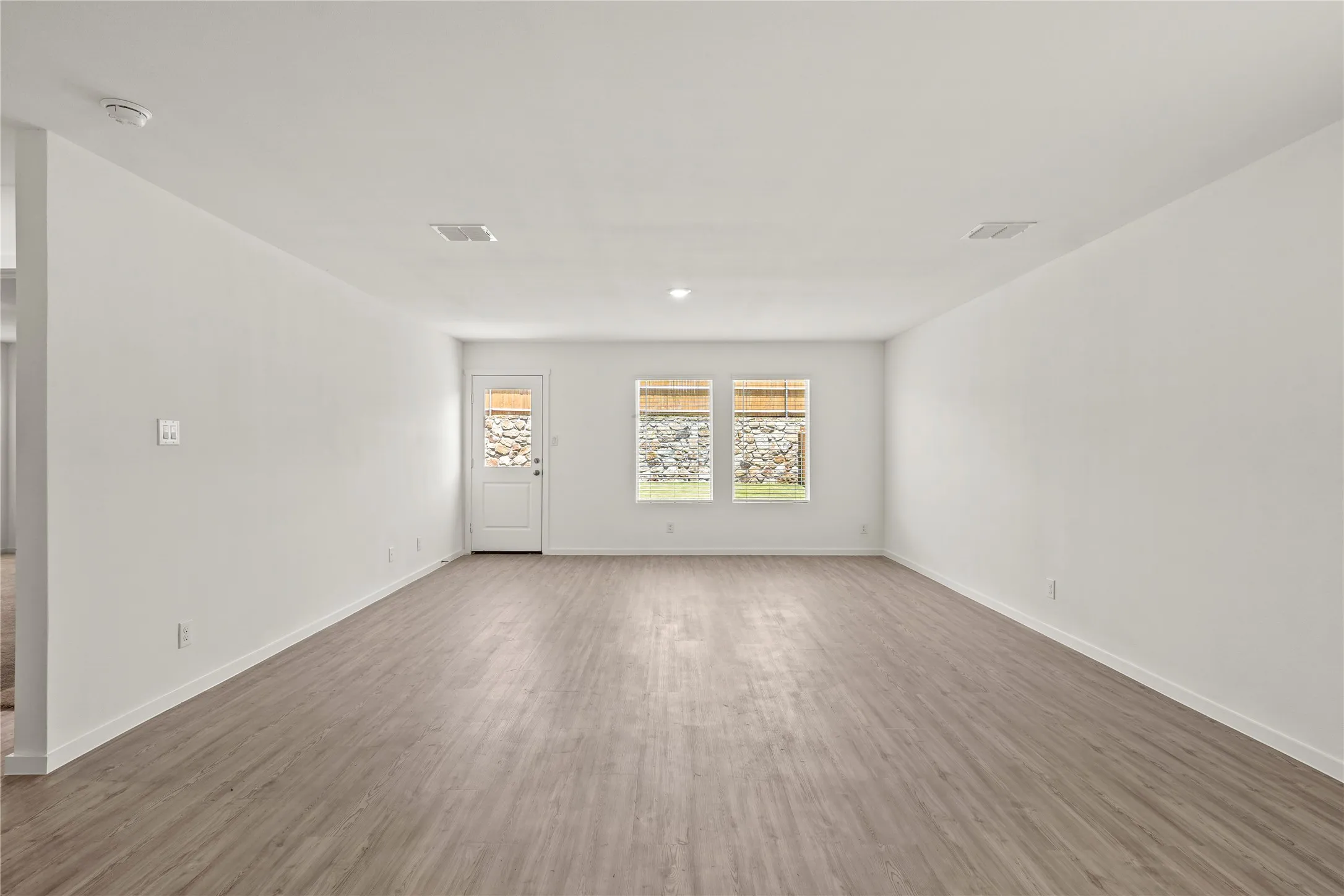 Spacious interior room featuring wood-finish flooring, white walls, and recessed lighting