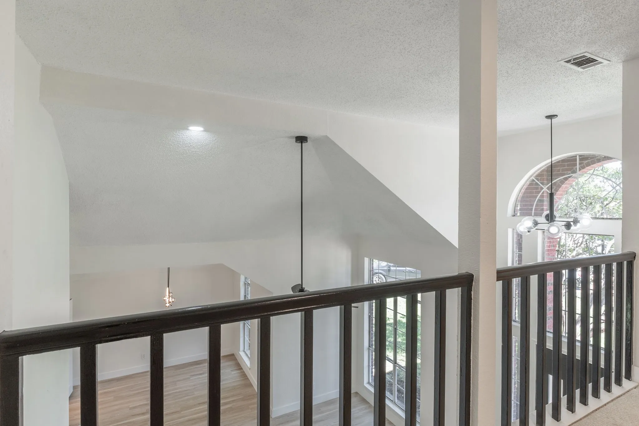 Overlooking space with dark wood railing, arched window, and two distinct pendant light fixtures