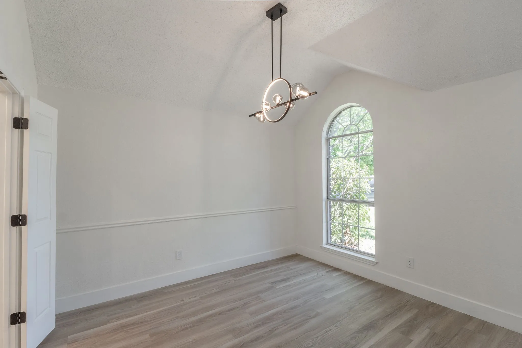 Interior space featuring an arched window, wood-finish flooring, a modern chandelier, vaulted ceiling, and chair rail molding