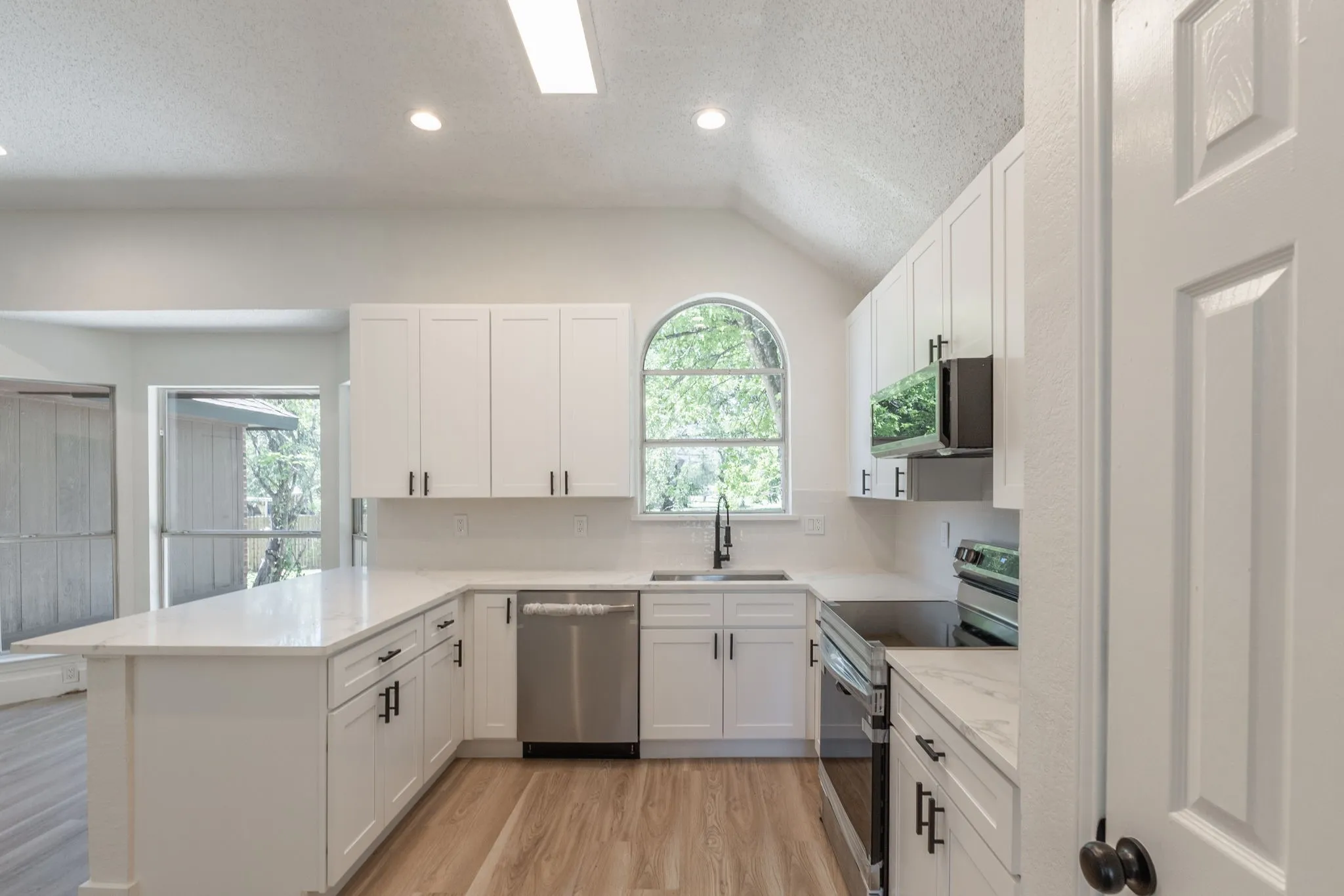 Modern kitchen featuring white cabinetry, light-toned countertops, stainless steel appliances, and wood-finish flooring