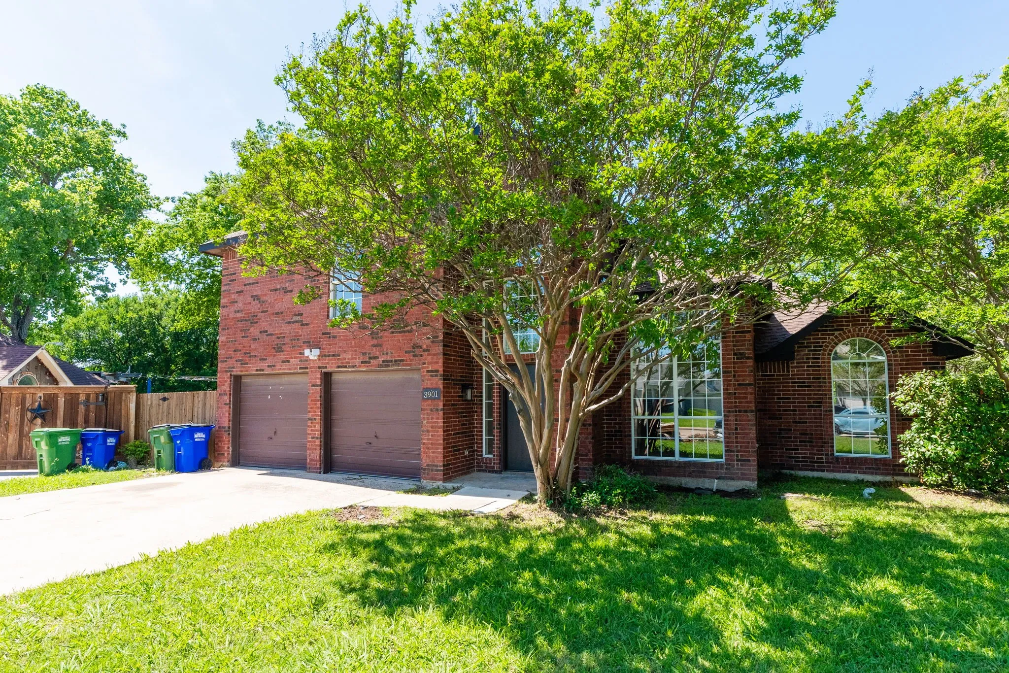 Red brick exterior with a two-car garage, mature trees, and an arched window accent