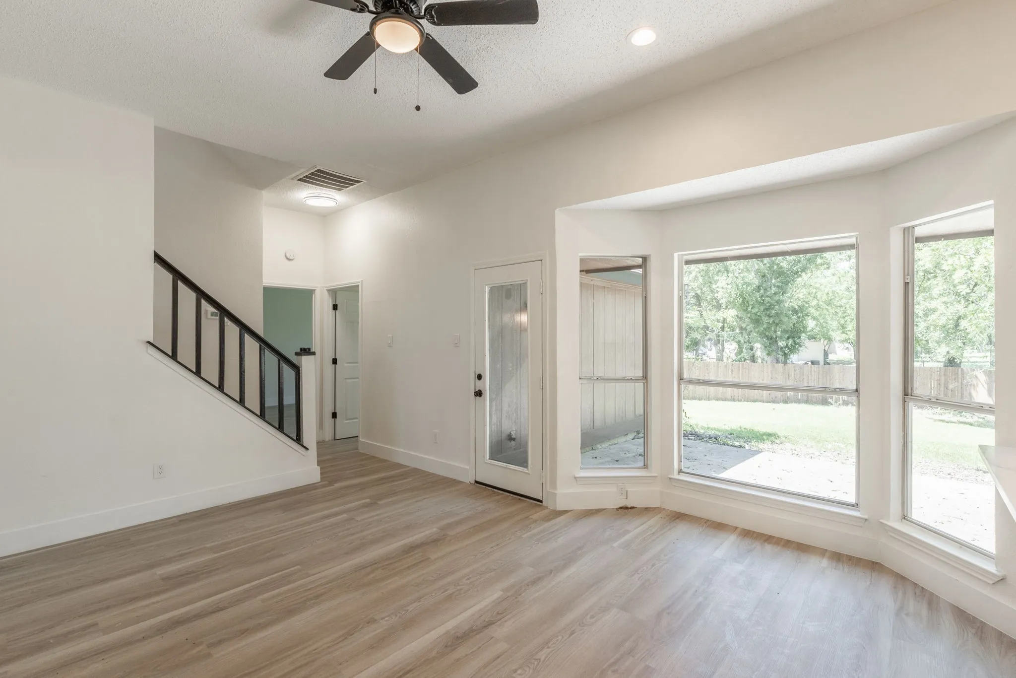Open-concept living area featuring wood-finish flooring, a contemporary ceiling fan, and a bay window with multiple panes