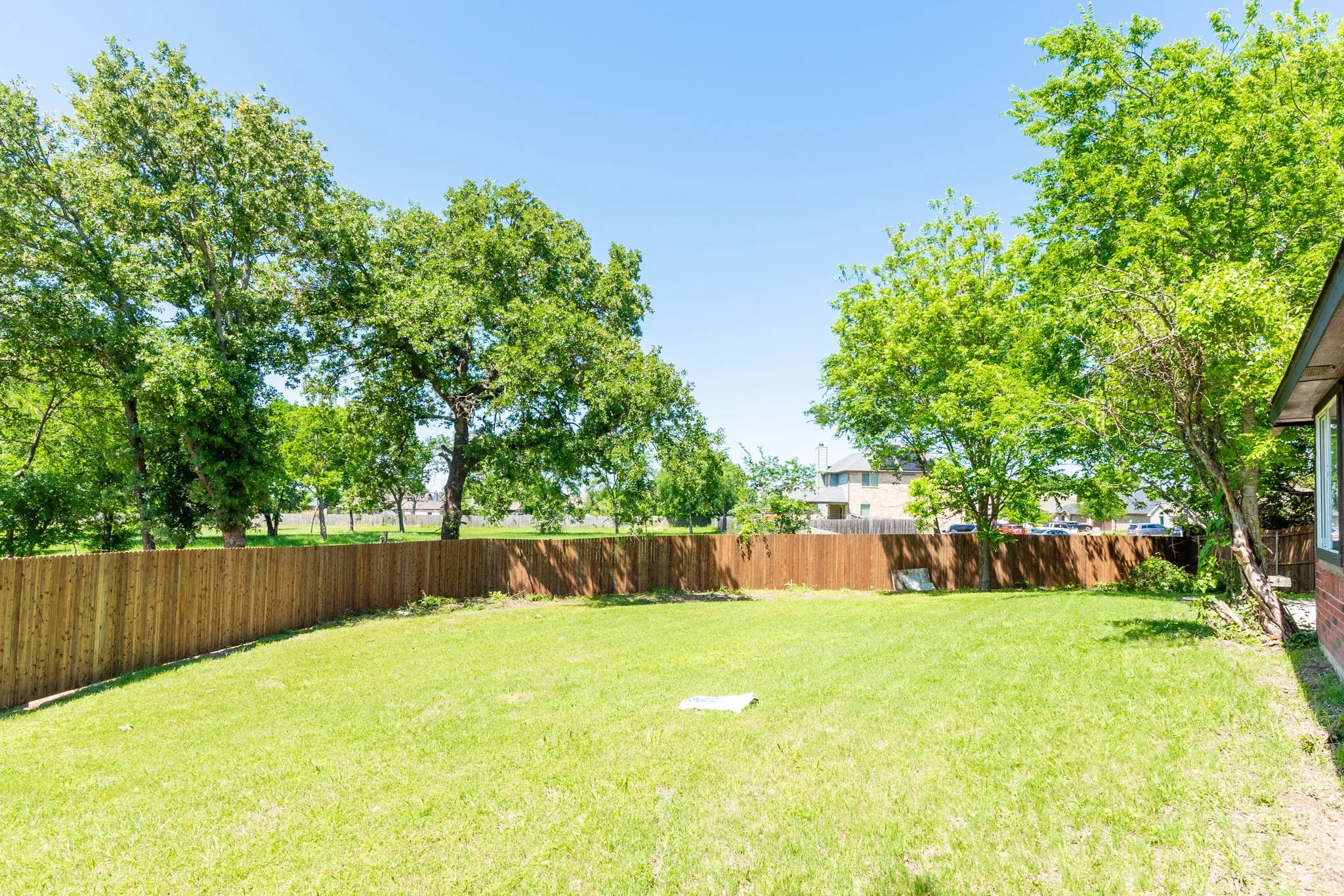 Spacious backyard featuring a privacy fence, mature trees, and a verdant lawn