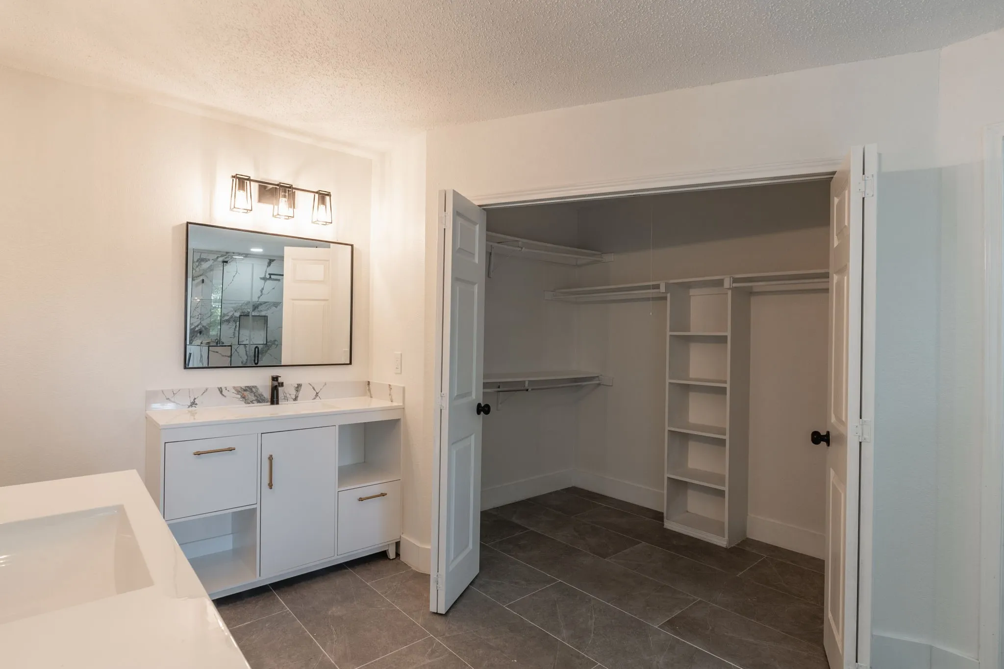 Spacious bathroom featuring a dual vanity with white cabinetry, a large mirrored cabinet, and a walk-in closet with built-in shelving