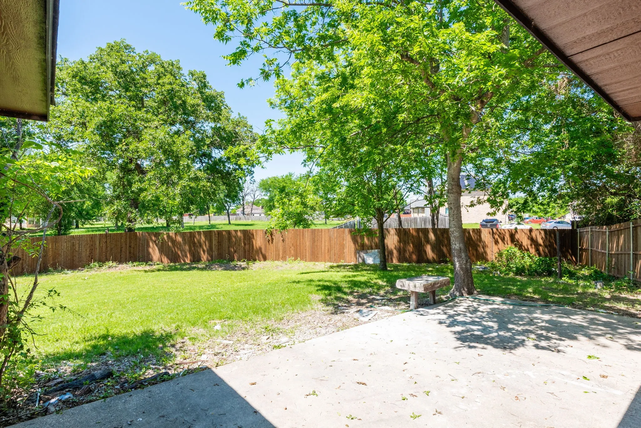 Expansive backyard featuring a concrete patio, mature trees, a manicured lawn, and wood privacy fencing