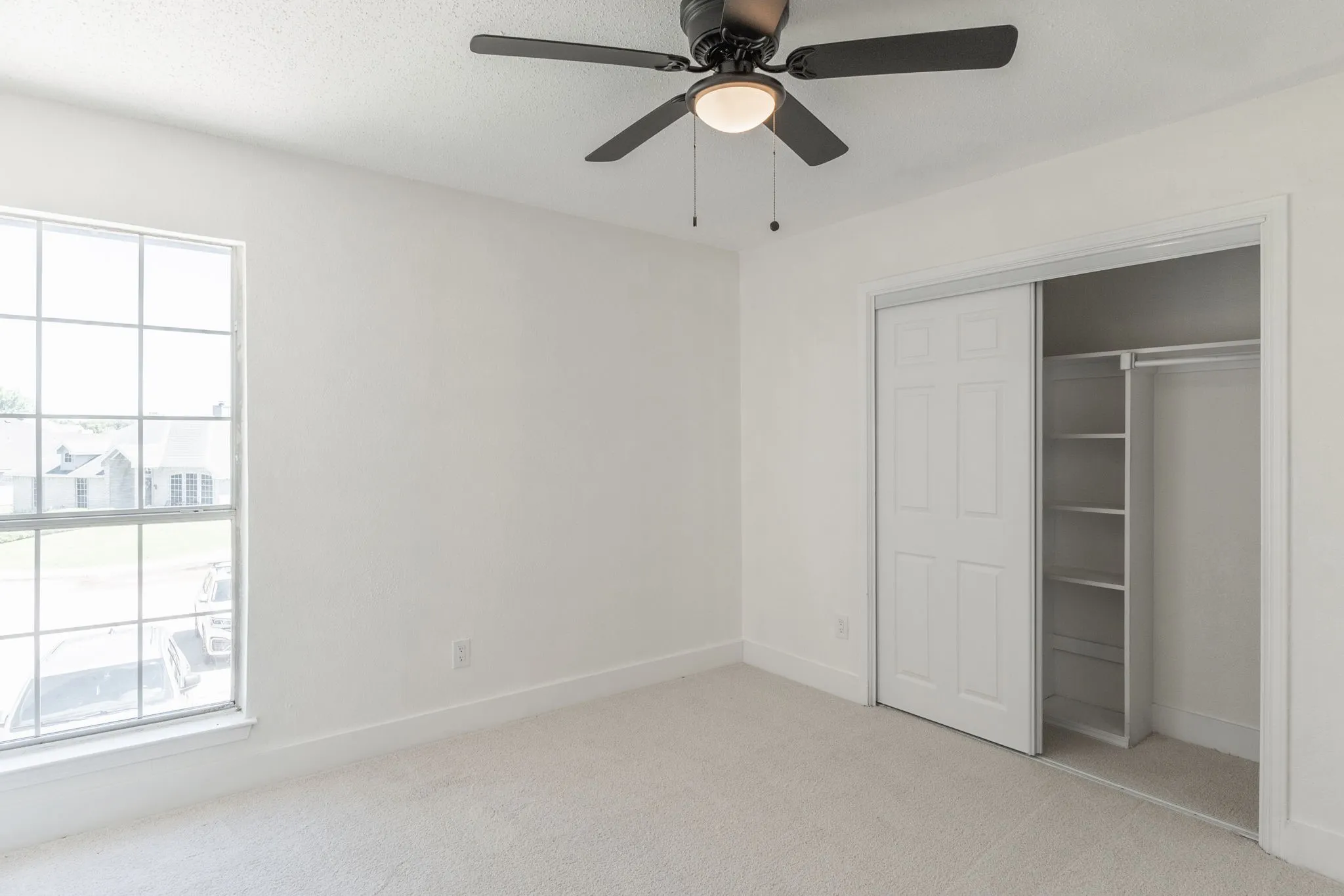 Bright room featuring a ceiling fan with light, plush carpet, and a large window with white trim