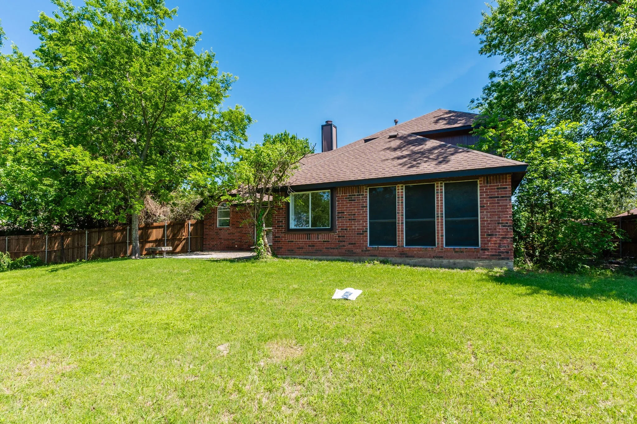 Spacious rear lawn with mature trees and a privacy fence