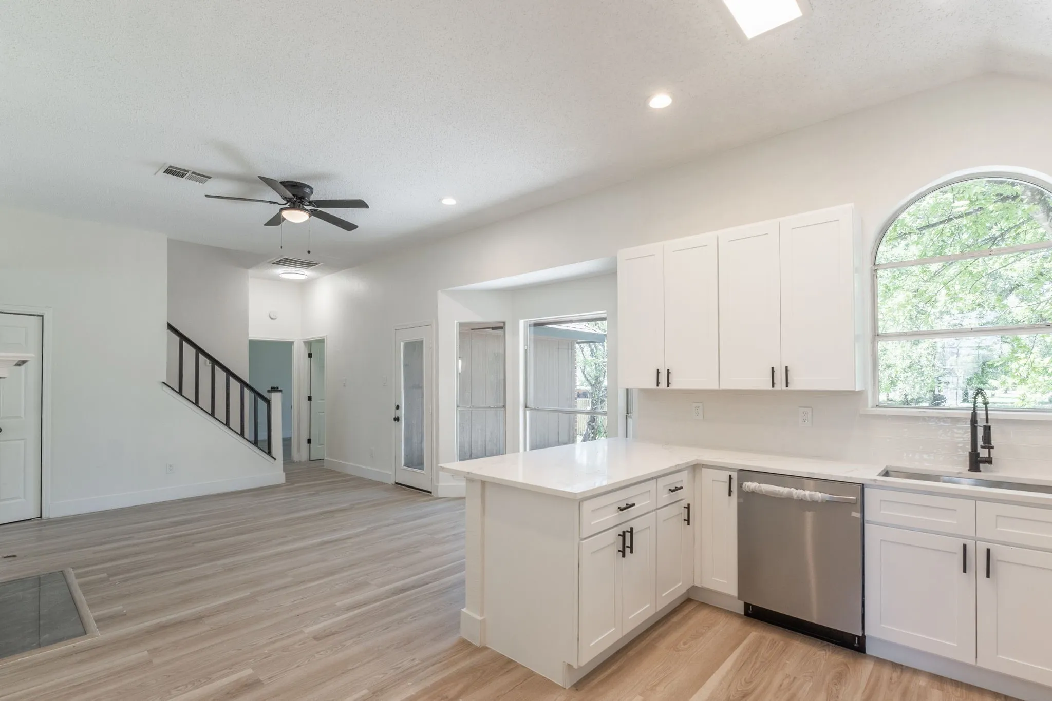 Modern kitchen featuring white shaker cabinetry, stainless steel appliances, and light-tone wood-finish flooring