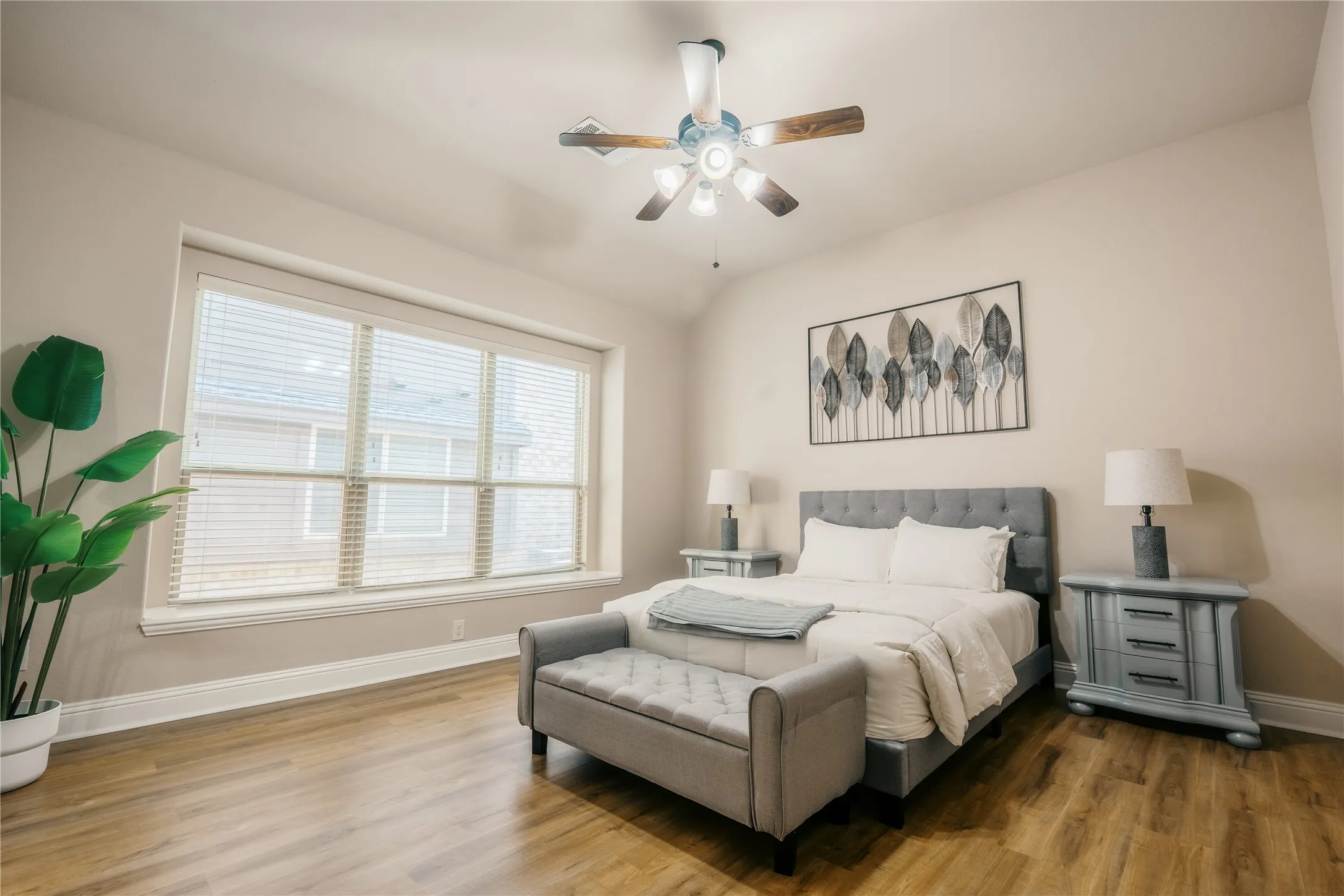 Spacious room featuring wood-finish flooring, a large window with blinds, and a ceiling fan with light fixture