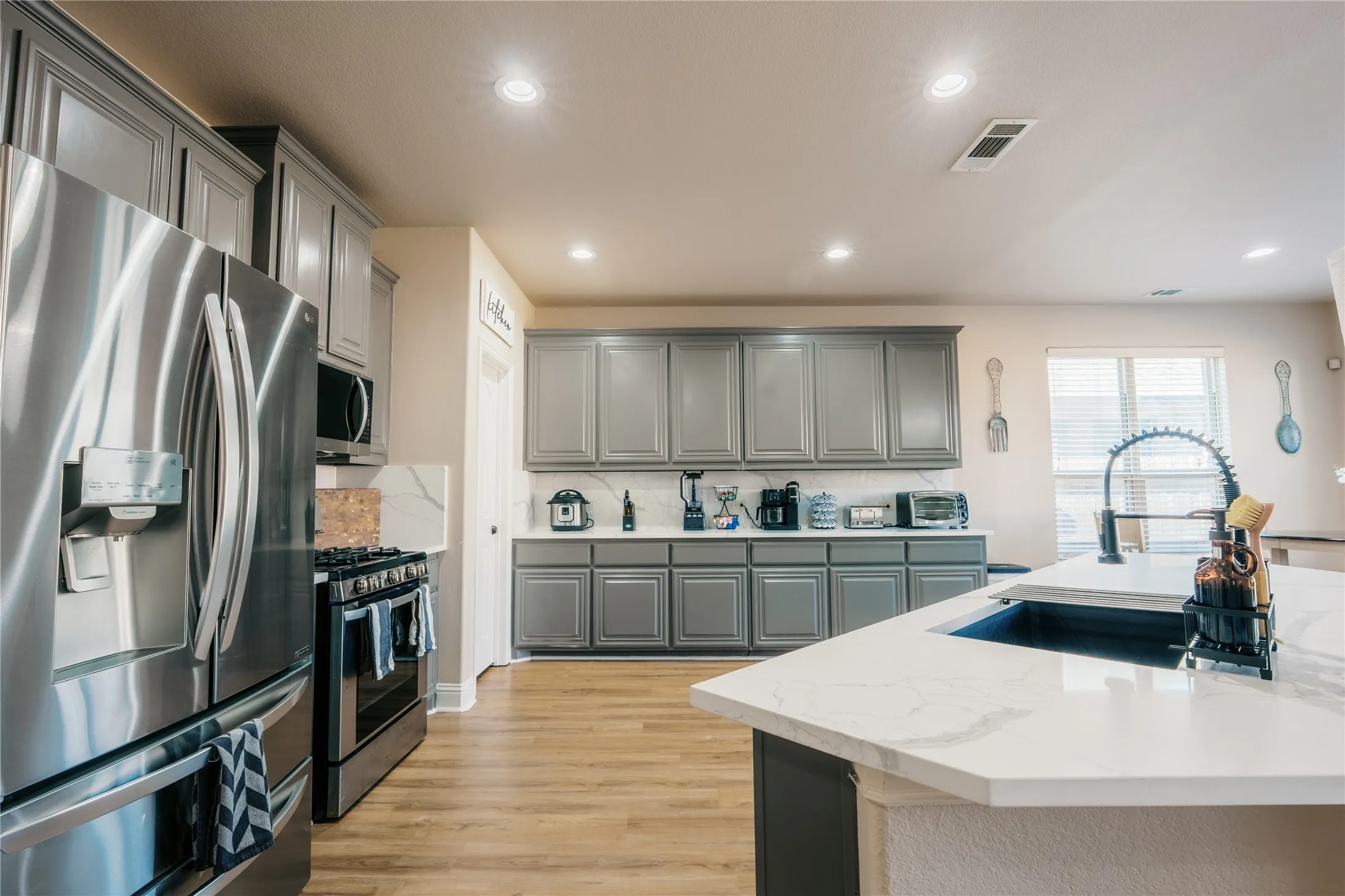 Modern kitchen featuring stainless steel appliances, grey cabinetry, light stone countertops, and wood-finish flooring