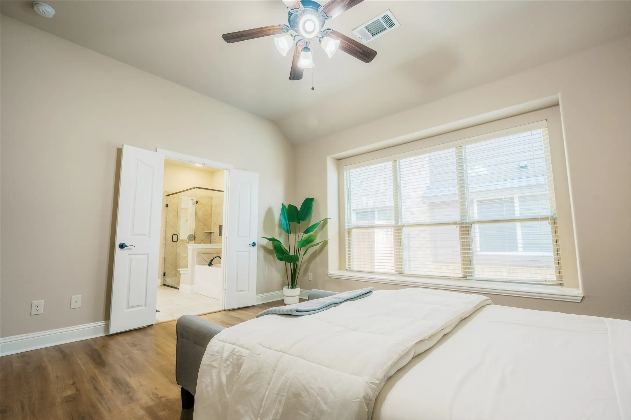 Bedroom featuring wood-finish flooring, a ceiling fan with integrated lighting, and a large window with blinds