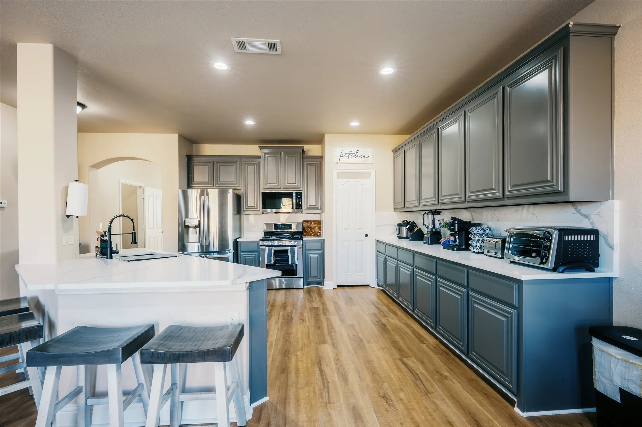 Open-concept kitchen featuring an island with seating, white countertops, gray cabinetry, stainless steel appliances, and wood-finish flooring