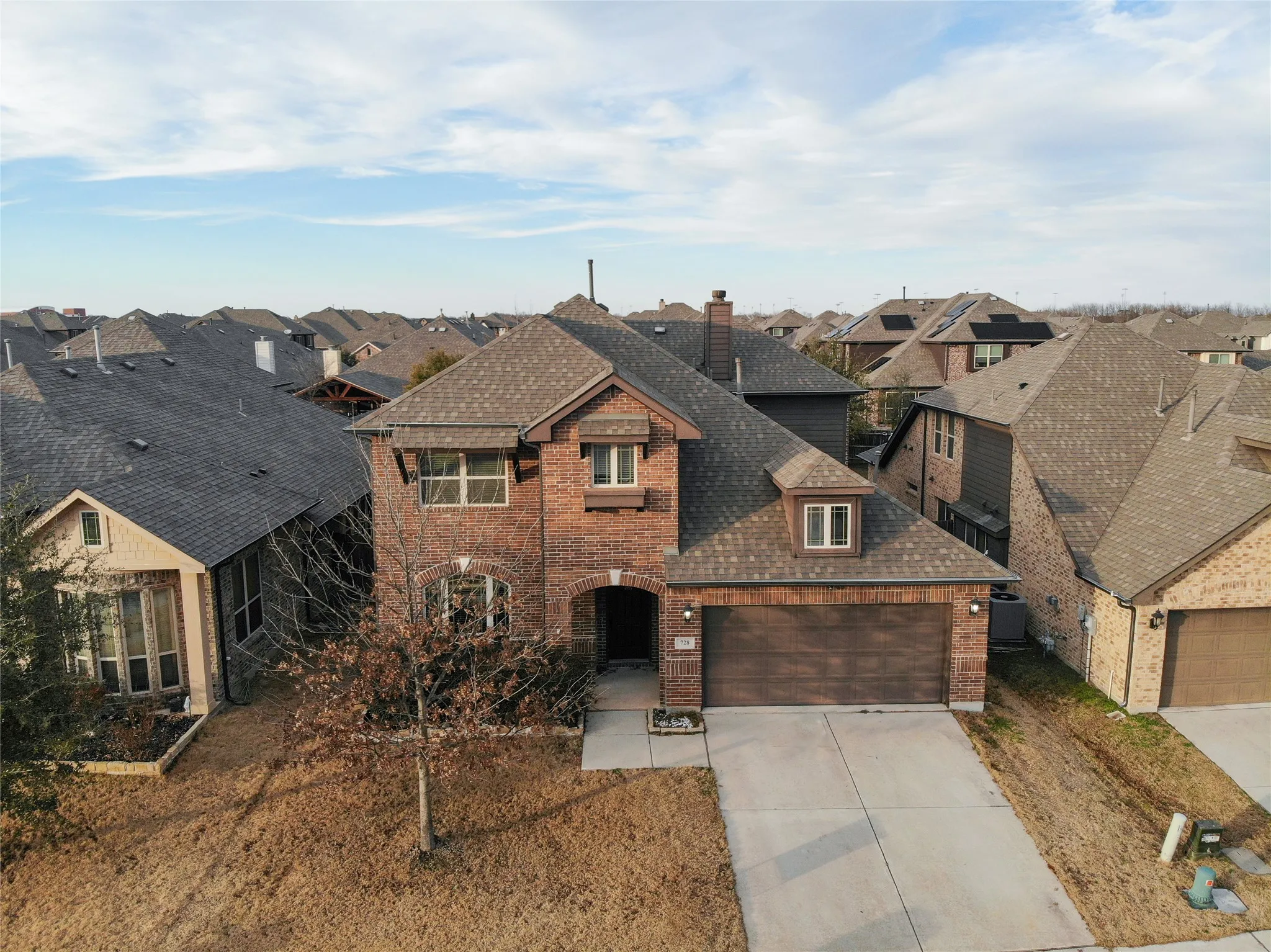 Brick facade residence featuring a two-car garage, dormer window, and mature landscaping