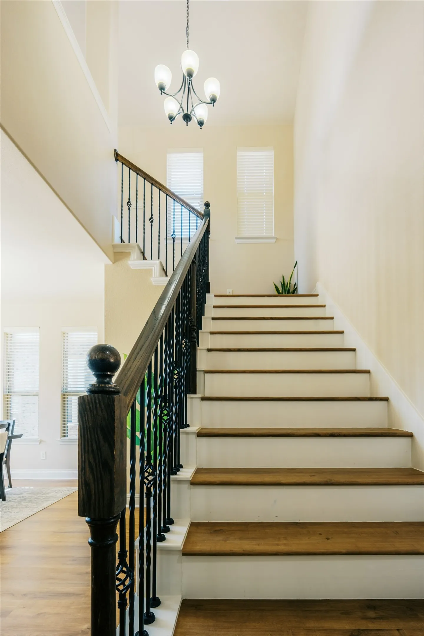 Staircase featuring wood-finish treads, white risers, a dark wood-finish handrail, and wrought iron balusters