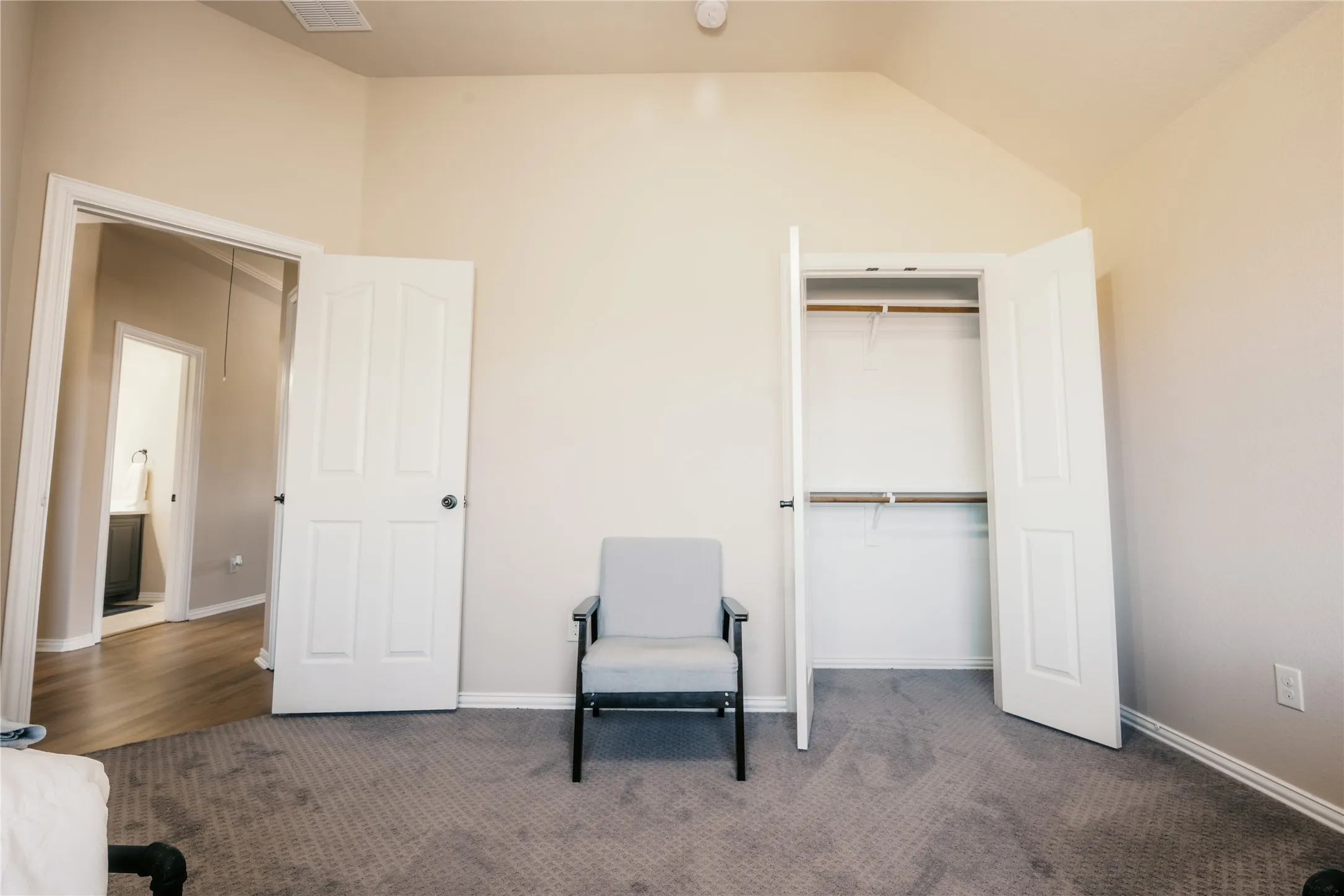 Carpeted room with a vaulted ceiling, a closet featuring bi-fold doors and dual hanging rods, and a paneled interior door leading to a separate area with wood-finish flooring