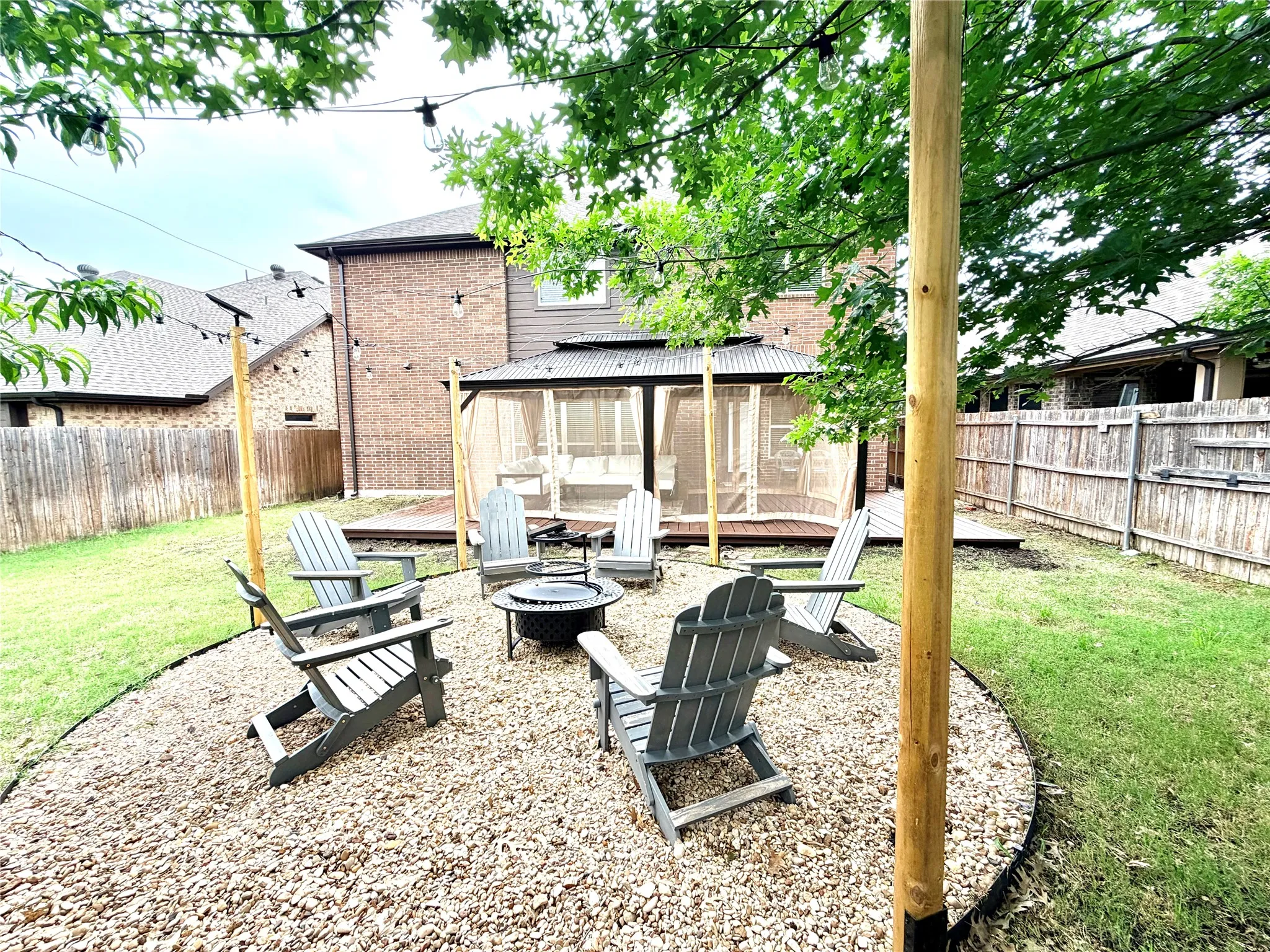 Backyard featuring a dedicated gravel fire pit area with string lights, a screened gazebo on a raised deck, and a grass lawn