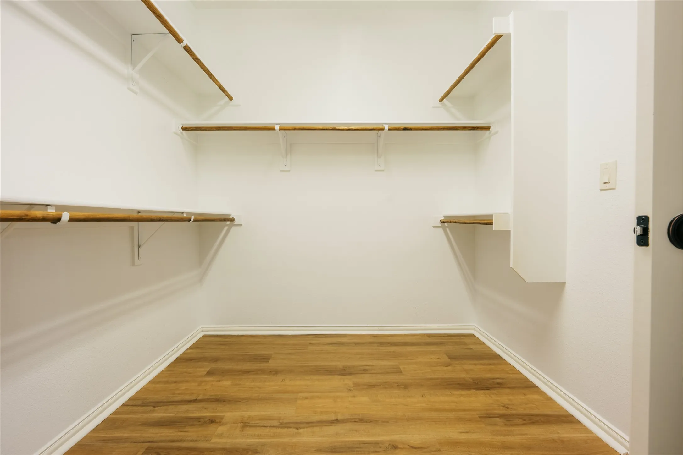 Walk-in closet featuring wood-finish flooring, white baseboards, white walls, and built-in shelving with hanging rods