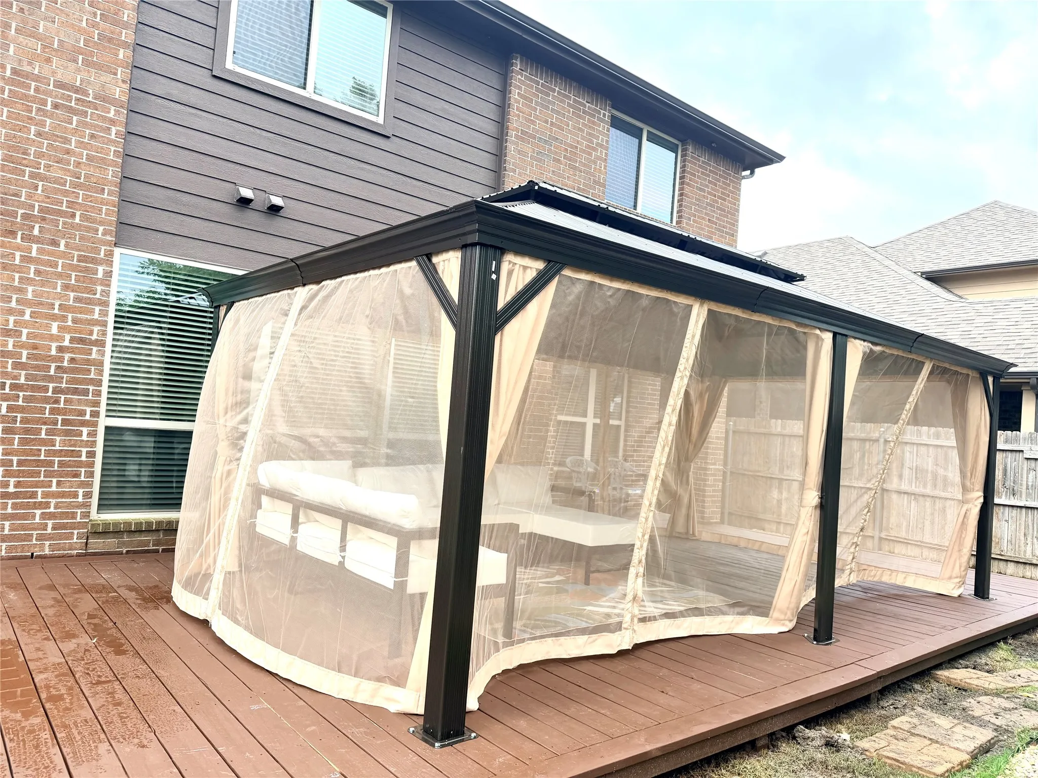 Expansive outdoor deck featuring composite decking, a gazebo with mesh and fabric screens, a brick exterior wall, and horizontal siding on the upper level
