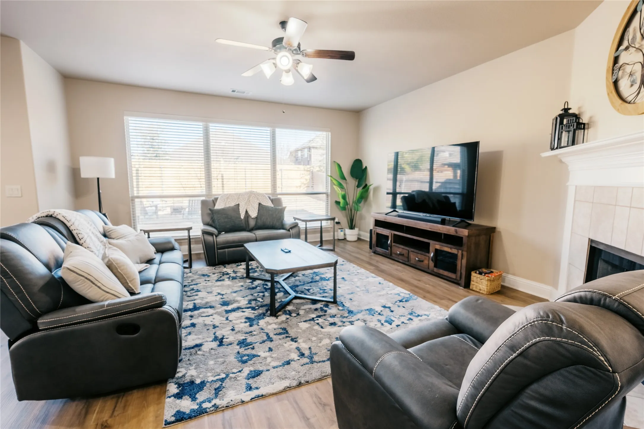 Spacious living room featuring wood-finish flooring, a ceiling fan with integrated lighting, and multiple windows providing ample natural light