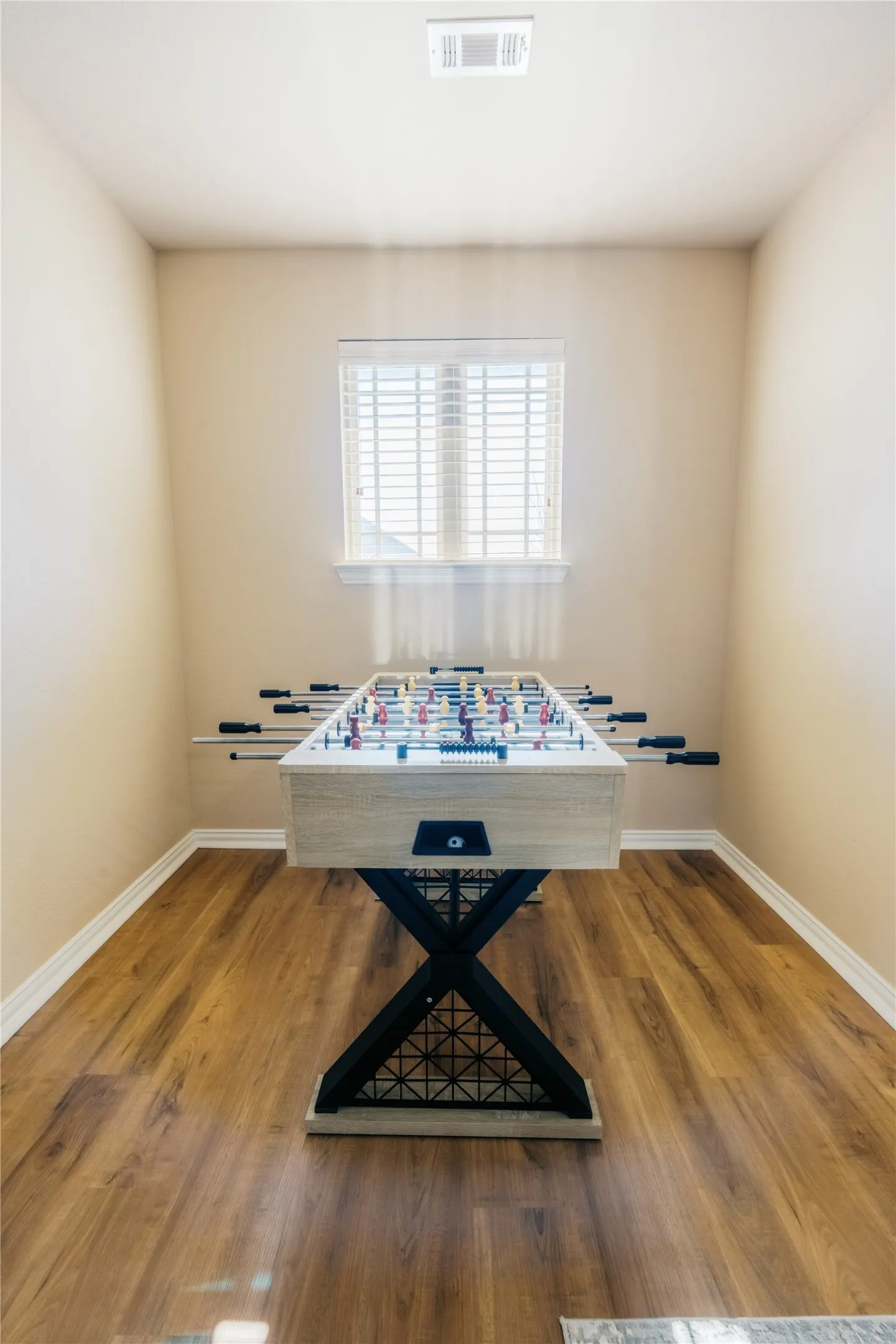 Bright room featuring wood-finish flooring, a single window with blinds, and neutral wall tones