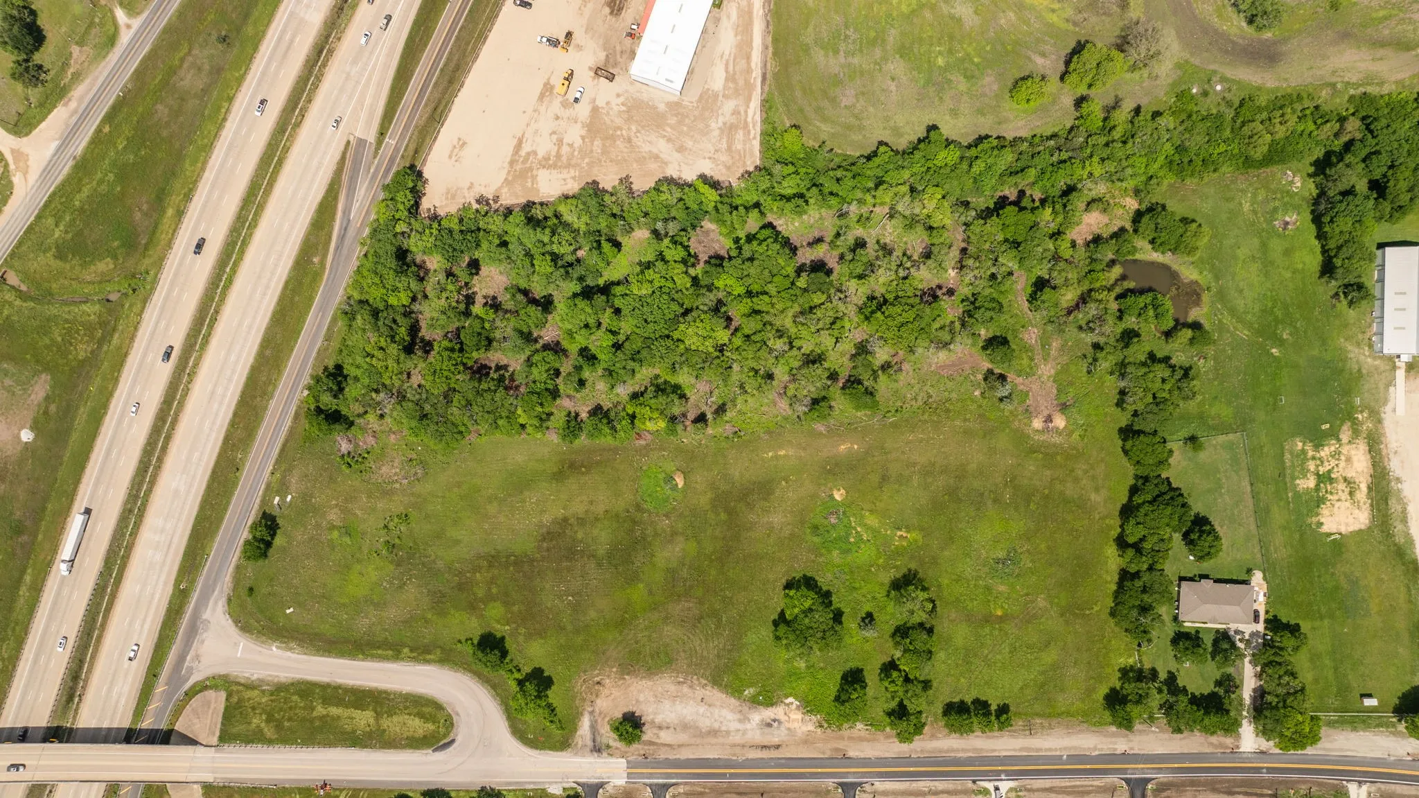 Expansive land parcel featuring direct highway frontage, cleared areas, mature tree lines, and a visible pond