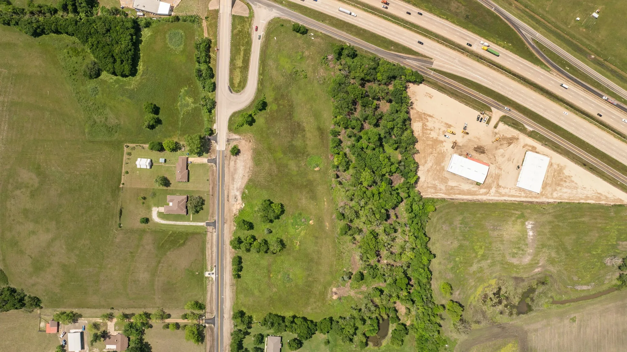 Aerial perspective of a verdant landscape featuring a major highway, a secondary road, and railway lines