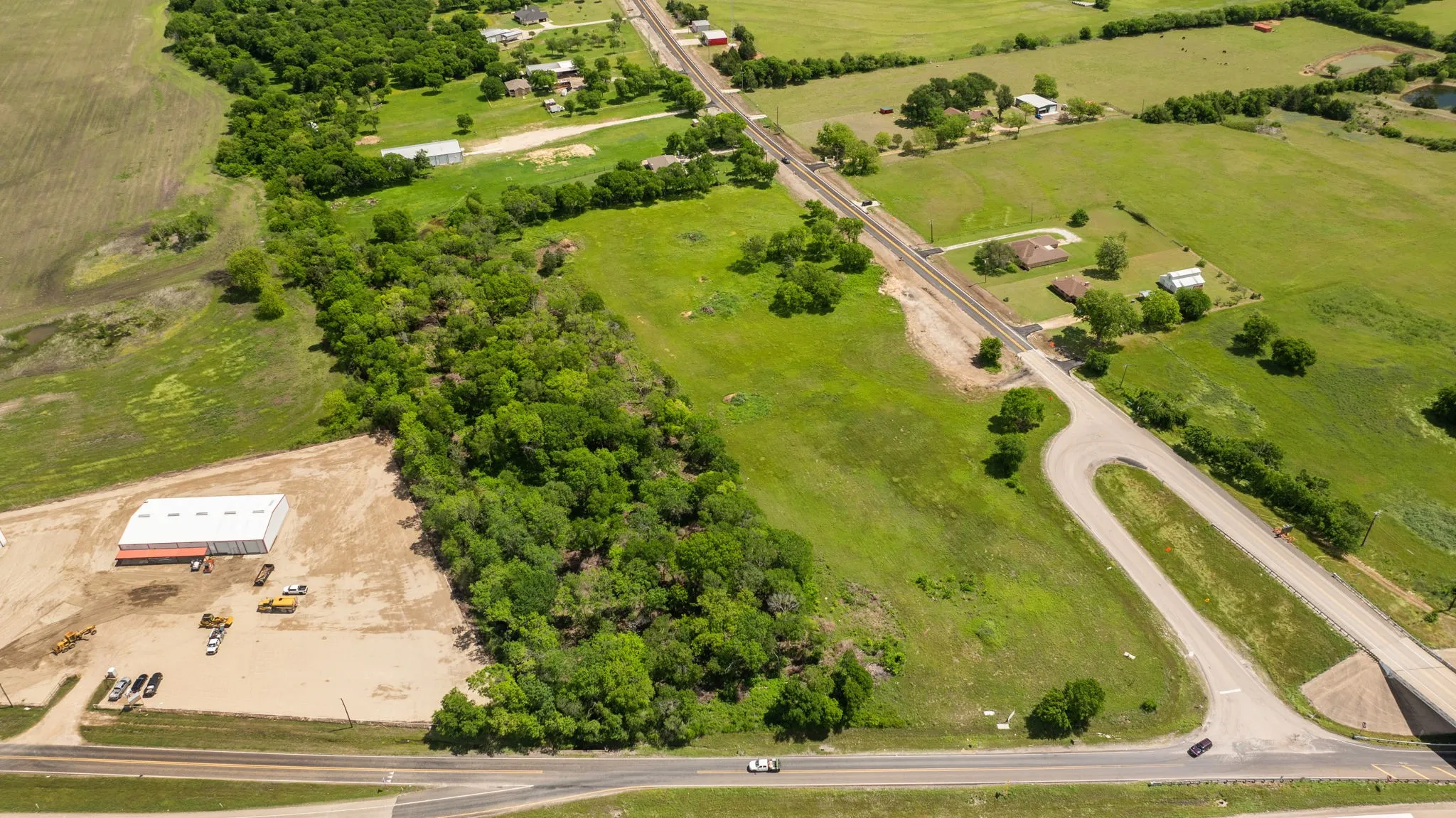 Expansive land parcel featuring a large commercial-style building with a light-colored roof and red trim, surrounded by undeveloped land