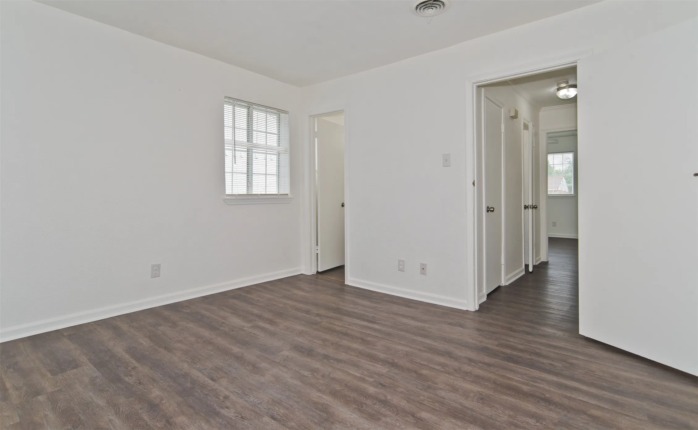 Spacious room featuring wood-finish flooring, white walls, and a window with horizontal blinds
